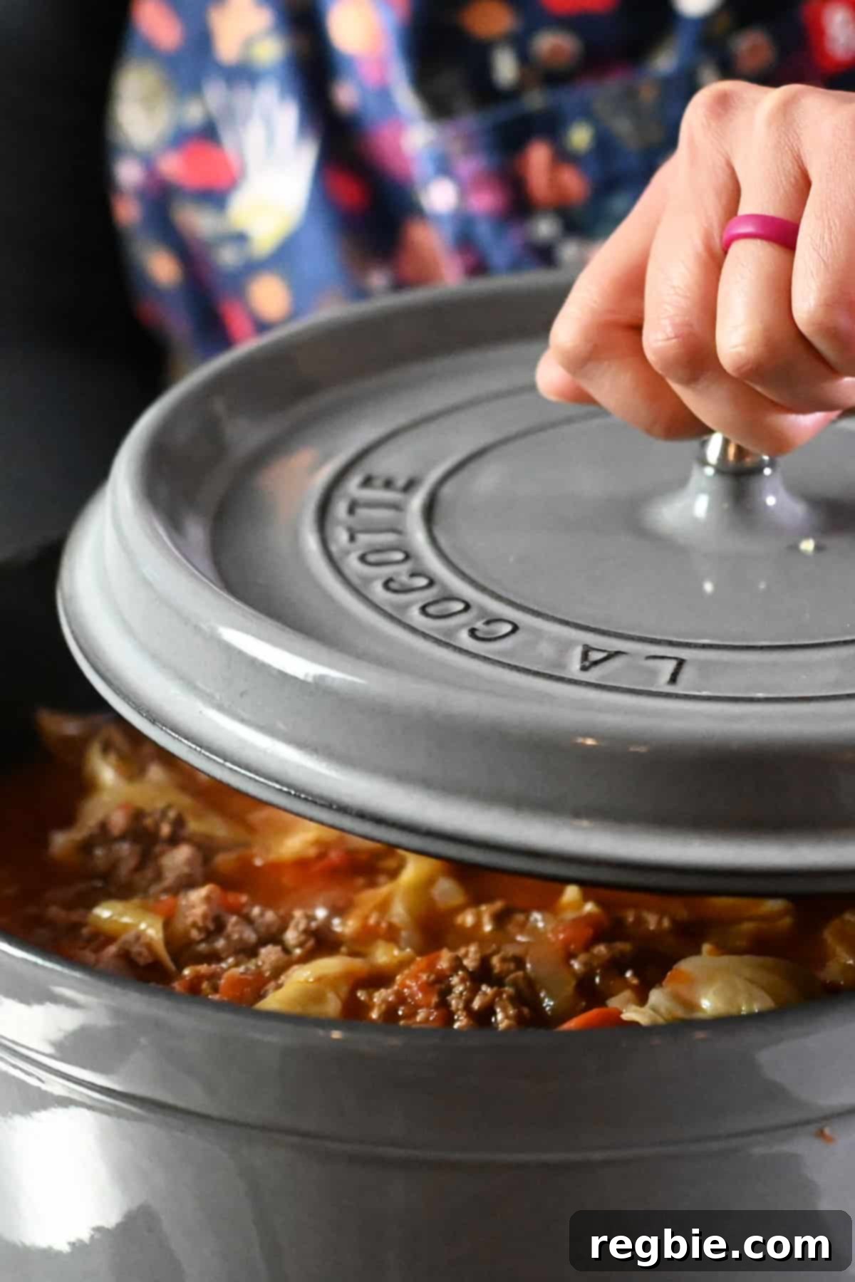 Removing the lid on a gray stockpot filled with cabbage roll soup, steam rising.