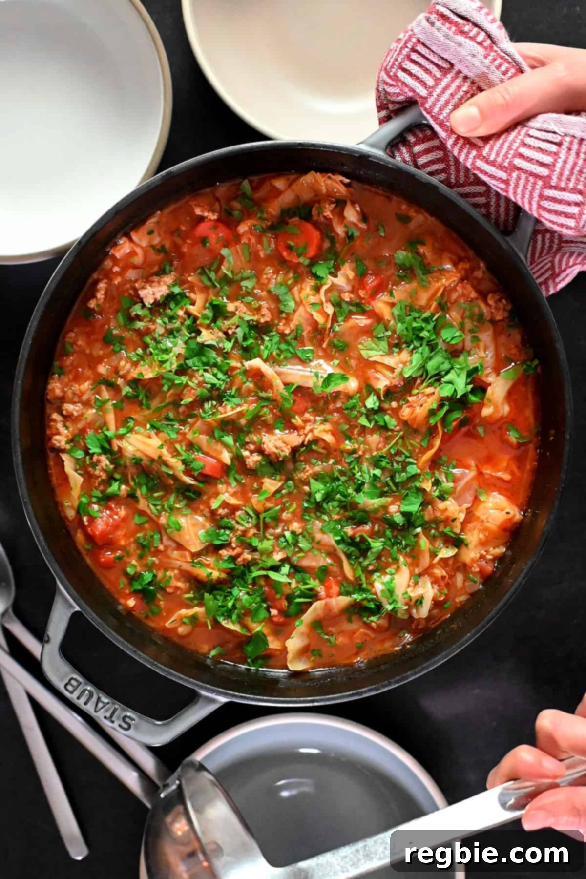 An overhead shot of a pot of cabbage roll soup topped with minced Italian parsley, next to some serving bowls and a ladle, ready to be served.