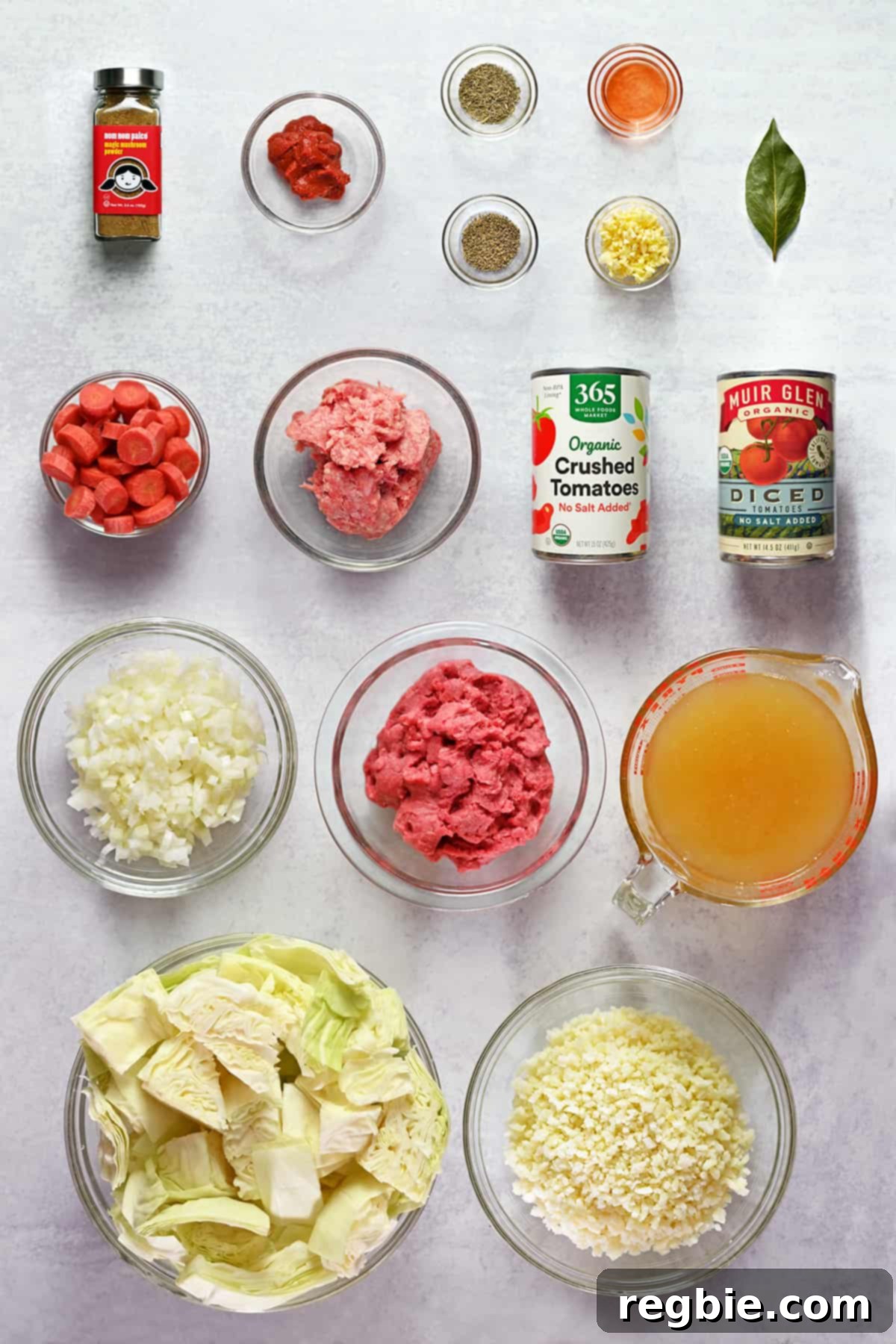 An overhead shot of the prepped ingredients to make unstuffed cabbage roll soup, including ground meat, various tomatoes, cabbage, carrots, and spices.