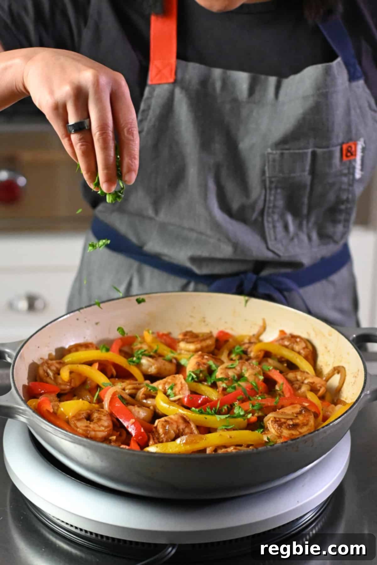 A chef's hand sprinkling fresh chopped cilantro over a sizzling skillet filled with colorful shrimp and bell pepper fajitas.