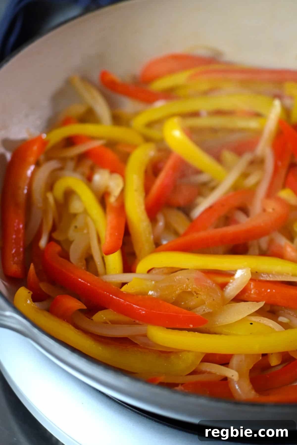 A detailed close-up shot of an enamel cast iron skillet, brimming with thinly sliced bell peppers and onions, perfectly sautéed for shrimp fajitas, showing light charring.
