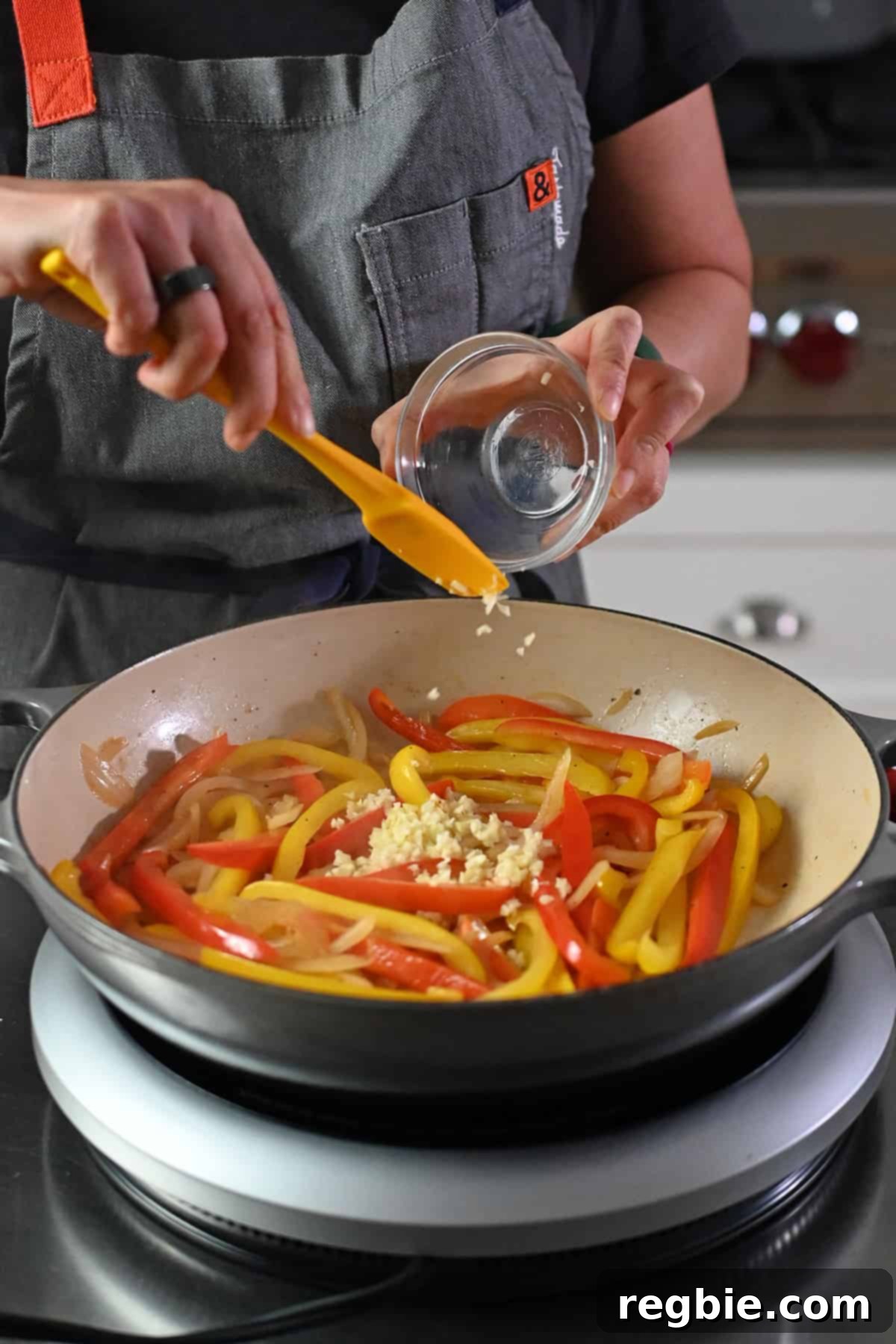 A hand adding minced garlic to a skillet already filled with vibrant, sautéed thinly sliced bell peppers and onions, enhancing the aroma and flavor of the fajitas.