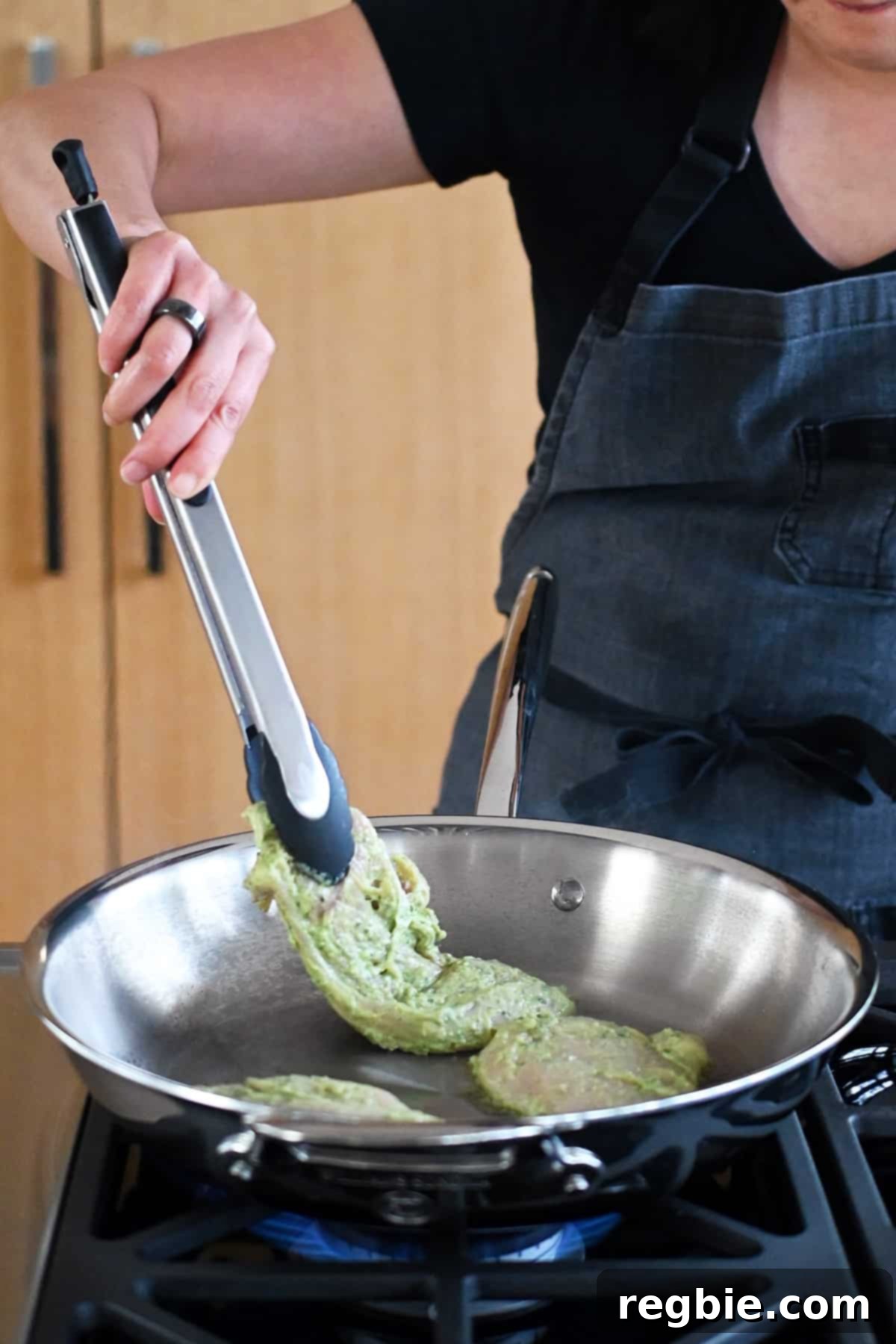 Savory Pesto Chicken 11 Adding pesto chicken to a stainless steel skillet with a pair of tongs.