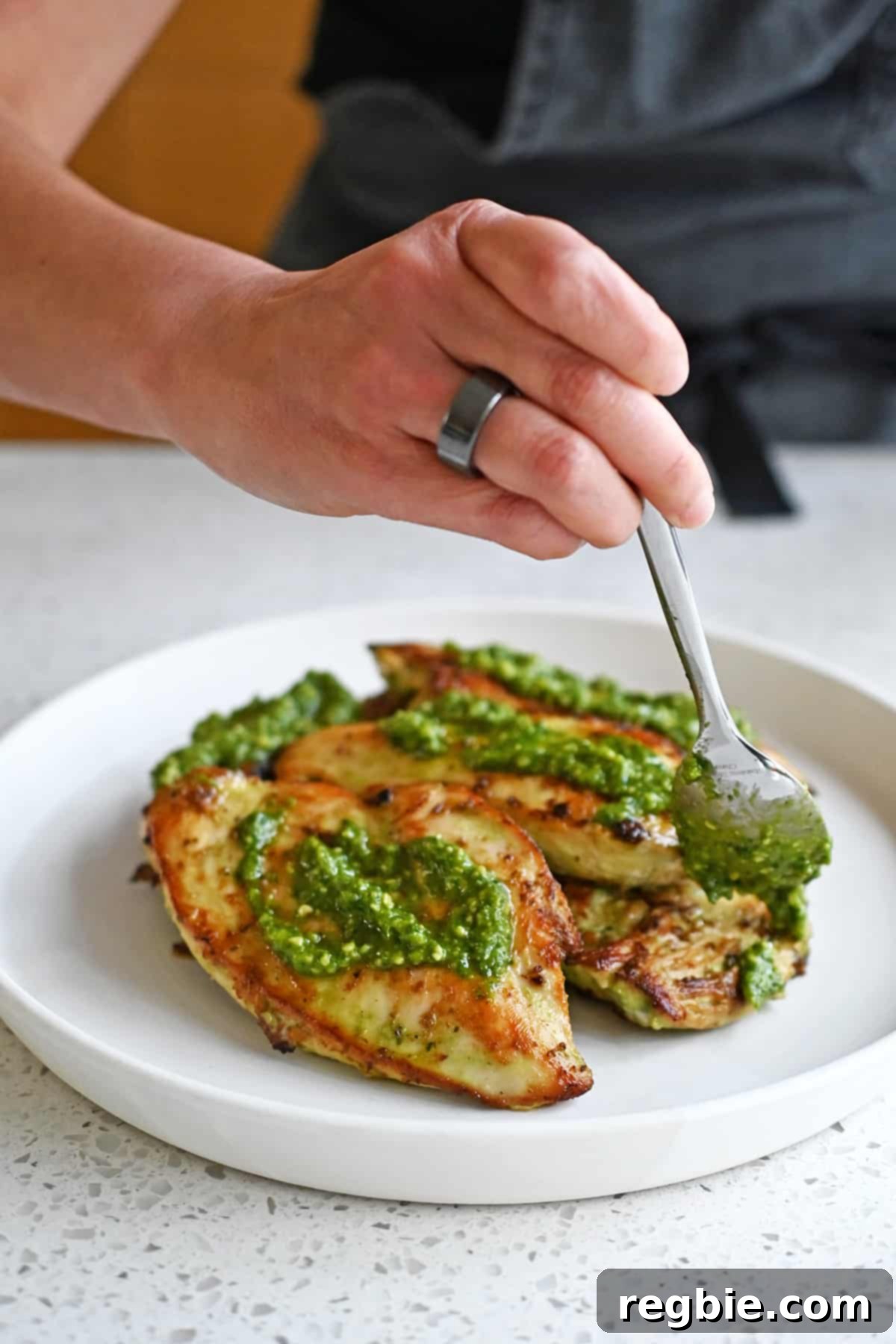 Savory Pesto Chicken 13 Spooning pesto onto a plate filled with pesto chicken cutlets right before serving.
