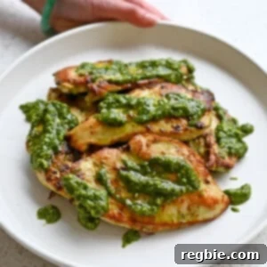 Savory Pesto Chicken 14 A hand is holding a white plate filled with pesto chicken cutlets topped with extra pesto.