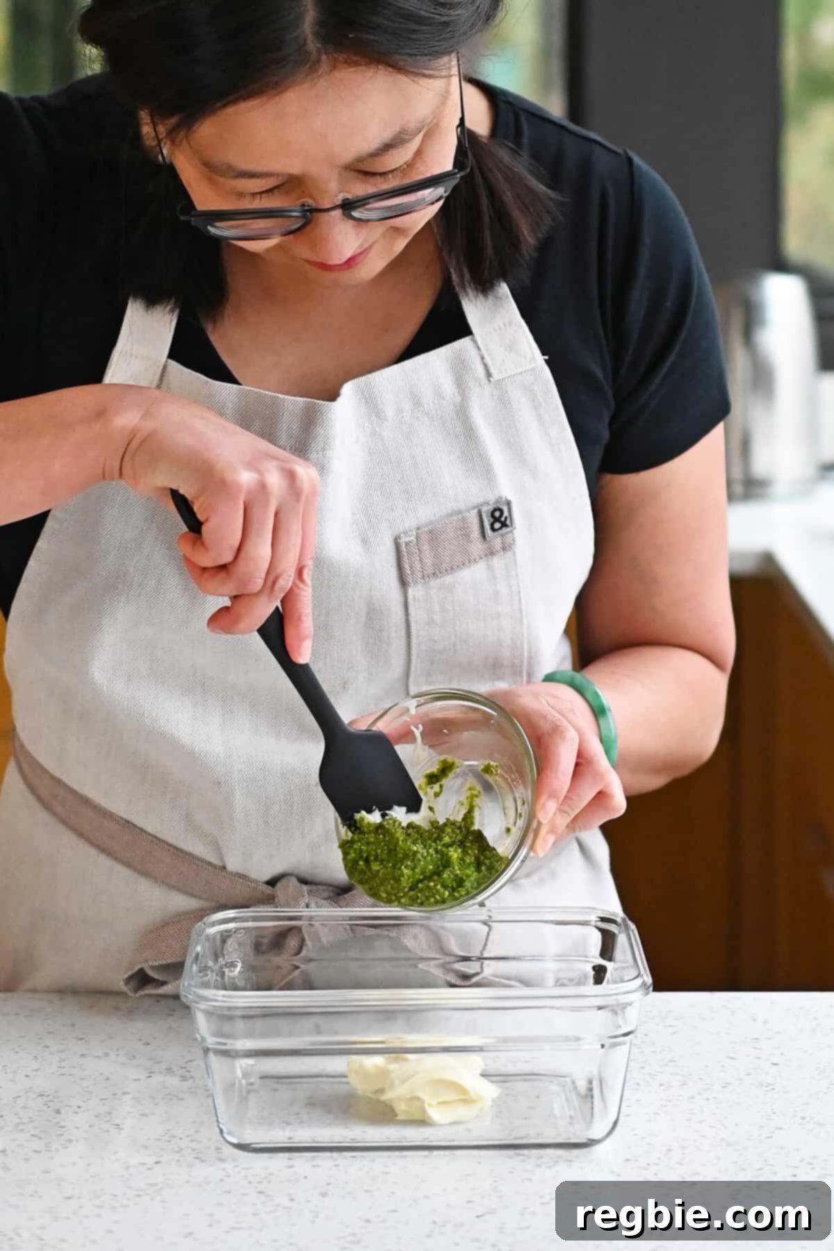 Savory Pesto Chicken 3 An Asian woman is adding fresh pesto to a glass container with some mayonnaise inside.