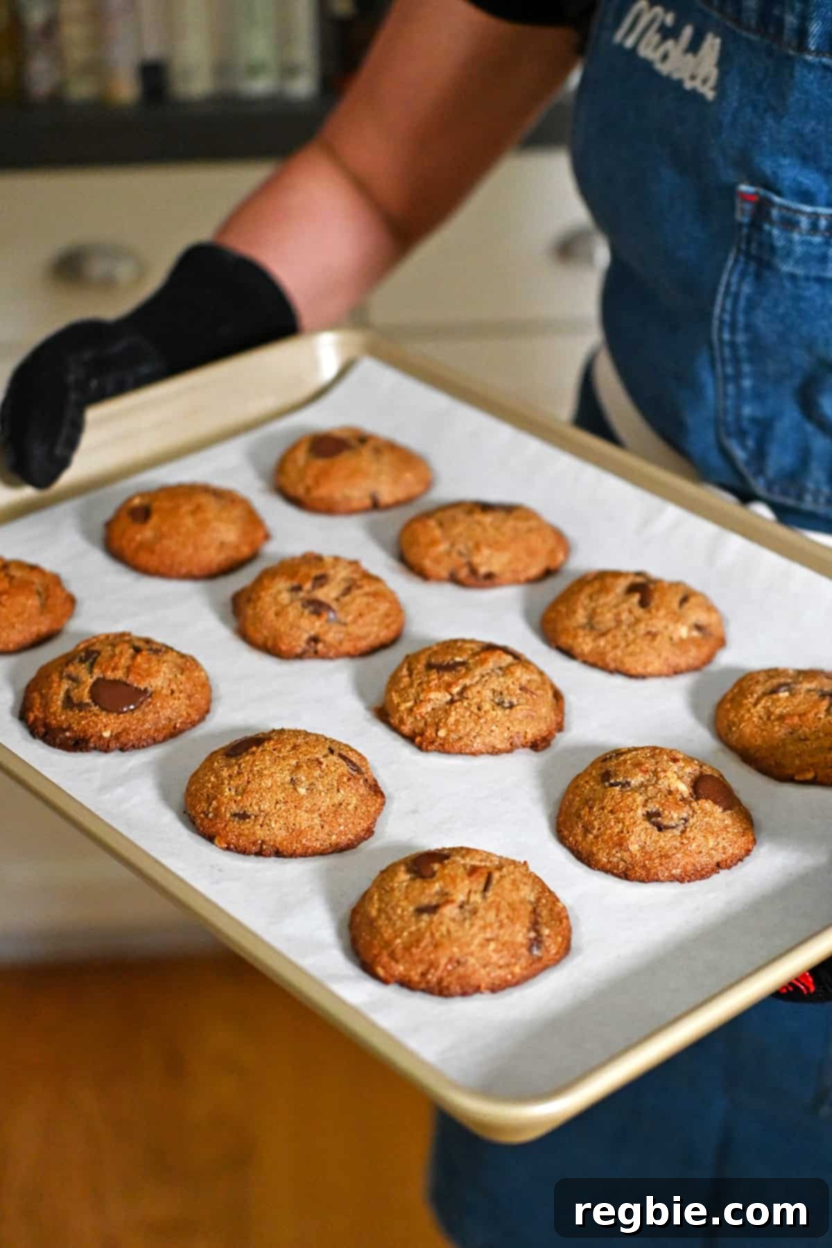 A person is holding a tray of freshly baked paleo banana chocolate chip cookies right out of the oven, showing their perfect golden-brown edges.