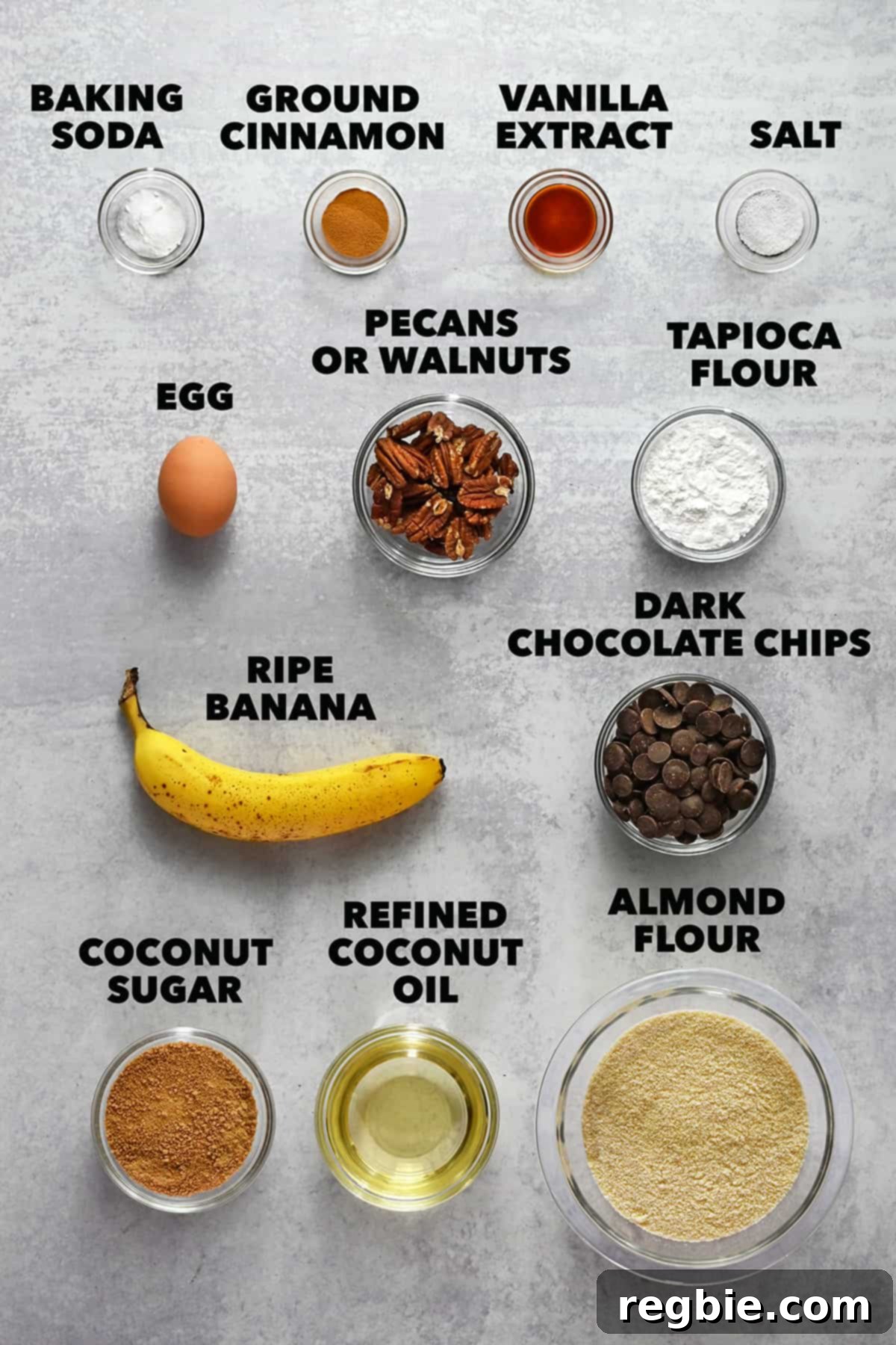 All the raw ingredients to make paleo banana cookies are measured out in small glass bowls, including almond flour, tapioca flour, coconut sugar, mashed banana, and chocolate chips.
