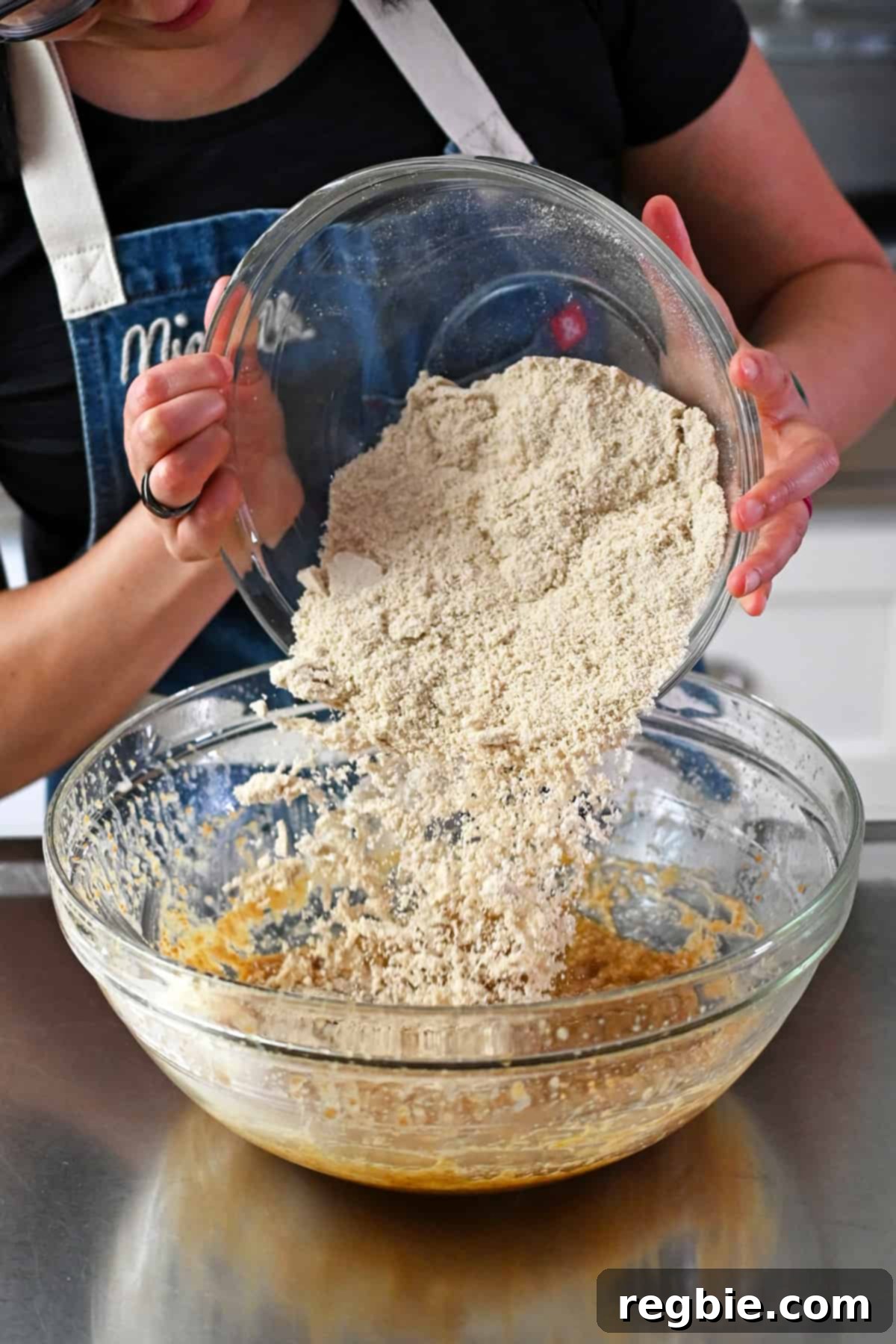 Adding the bowl of dry ingredients to the glass mixing bowl of wet ingredients to make paleo banana cookies.