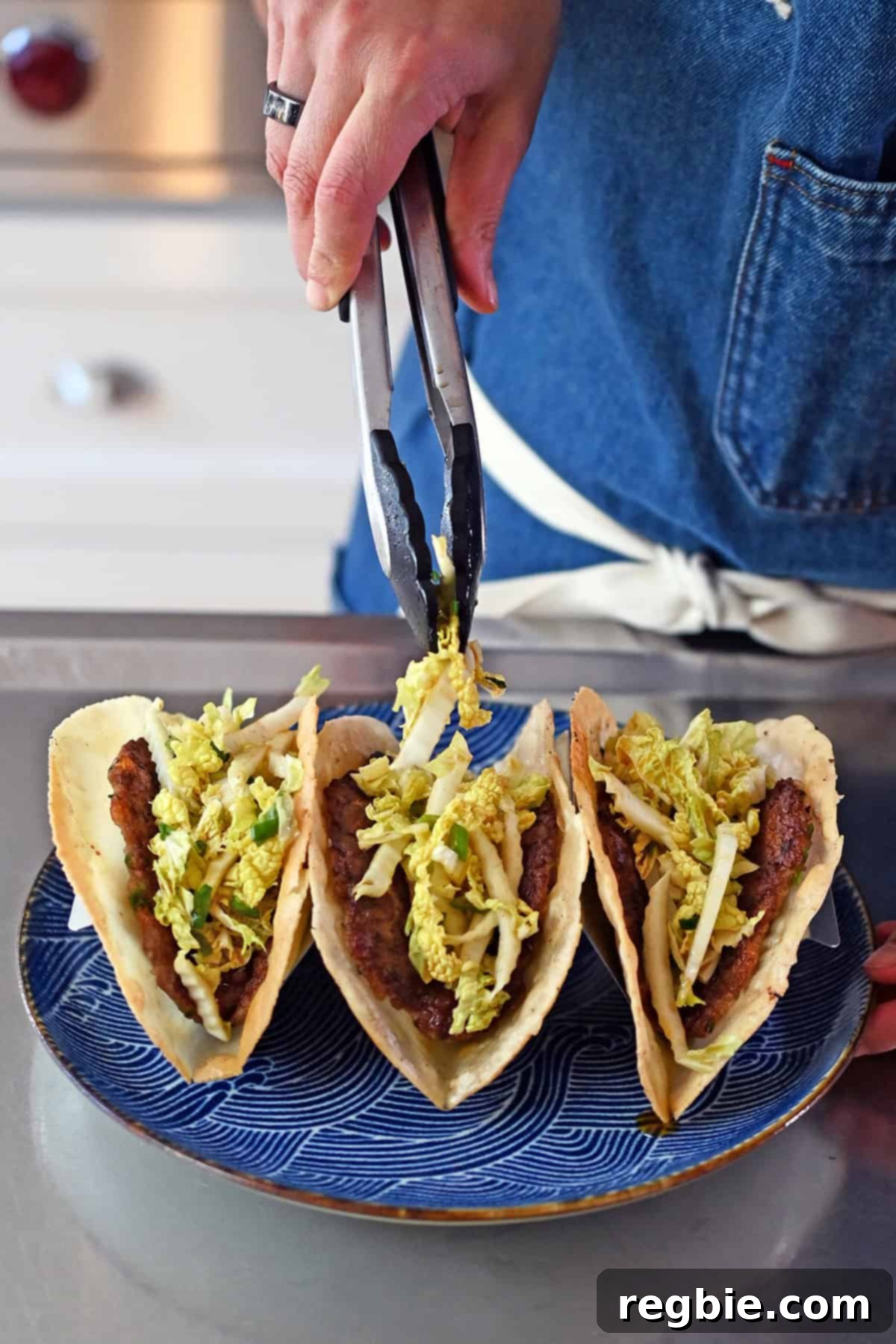 A close-up shot of seasoned Napa cabbage slaw being artfully added as a topping to a line of freshly made smash dumpling tacos.