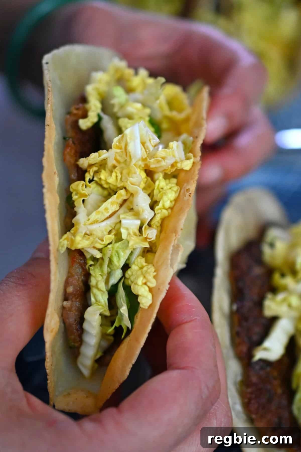 A detailed close-up of a perfectly constructed smash dumpling taco, generously filled with a vibrant Napa cabbage slaw, held delicately by two hands, ready for a delicious bite.
