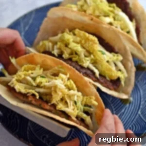 Two hands are picking up a dumpling smash taco from a blue plate filled with three of them.