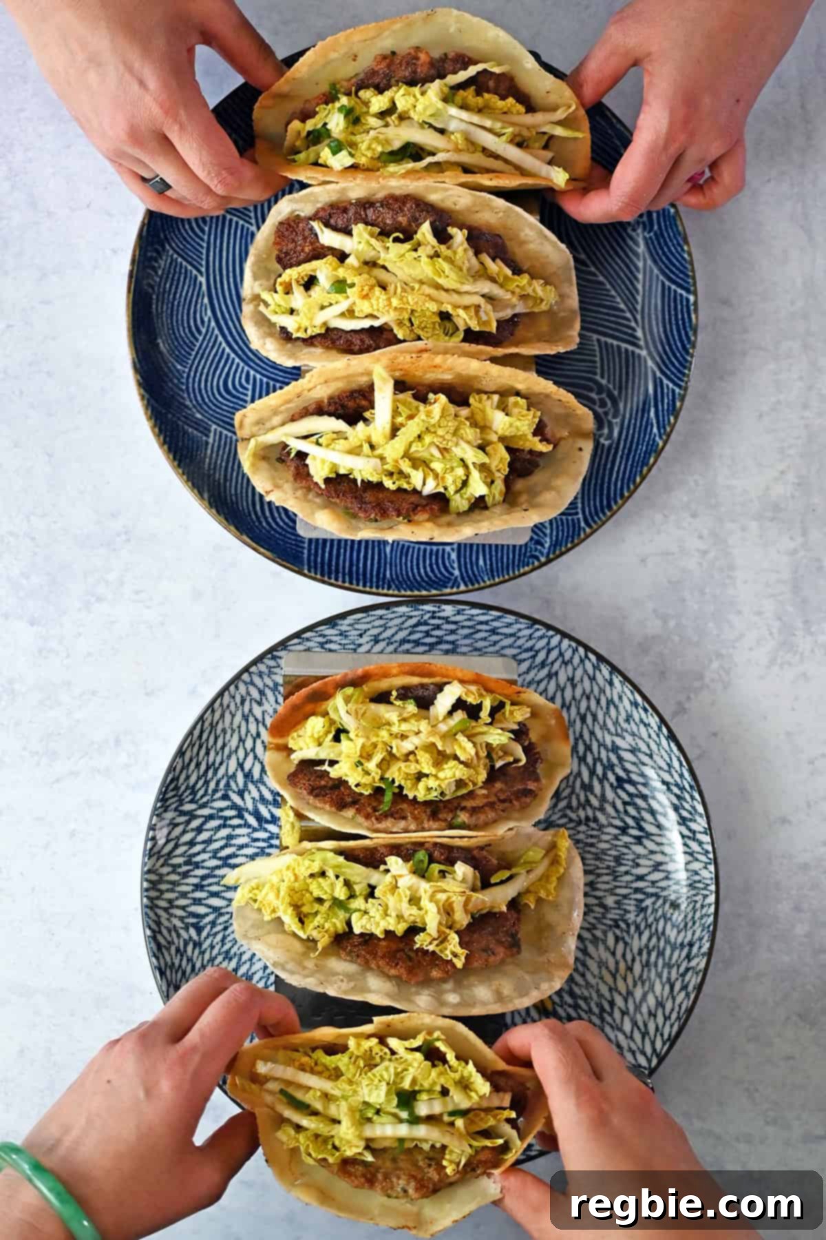 An inviting overhead view of two plates, each holding three perfectly formed smash dumpling tacos. A pair of hands reaches in to pick up one taco from each plate, highlighting the ease of serving and the deliciousness of this Asian-inspired dish.