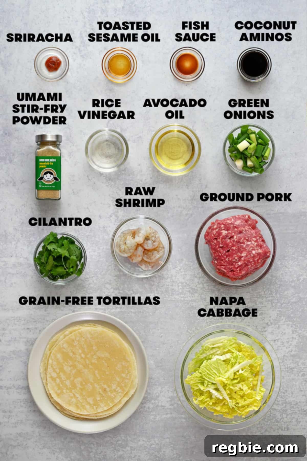 An overhead flat lay of all the raw ingredients neatly arranged for making paleo and gluten-free smash dumpling tacos, including ground pork, shrimp, fresh herbs, and various sauces.