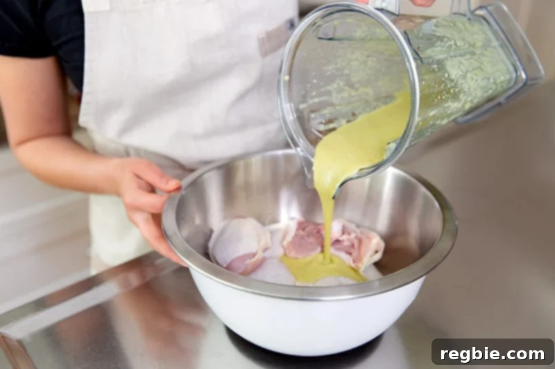 Pouring the paleo & Whole30 Asian chicken marinade over chicken thighs in a white stainless steel bowl.