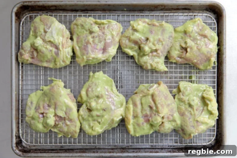 An overhead shot of marinated thighs arranged on a wire rack in a rimmed baking sheet with the skin-side down.