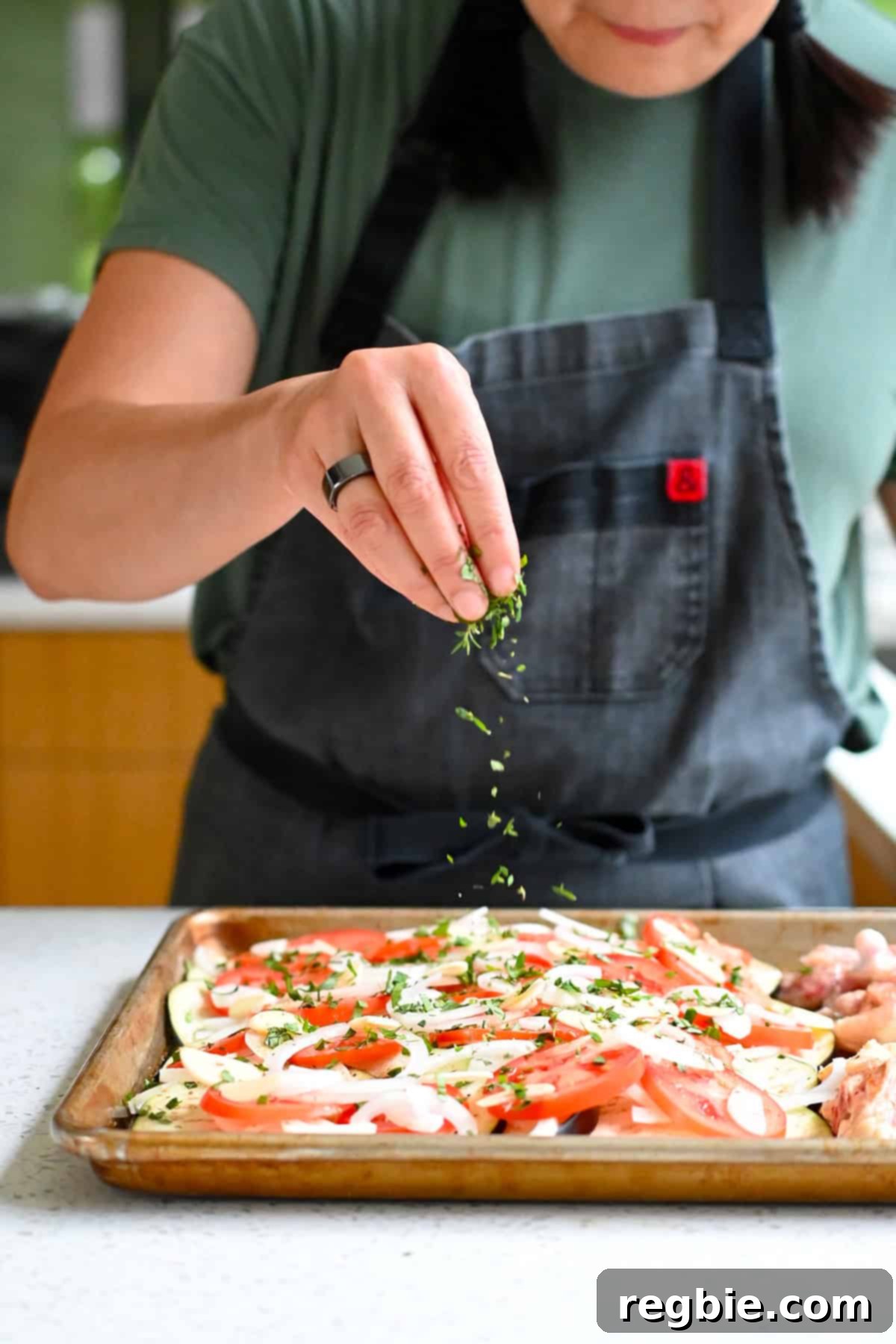 Sprinkling minced fresh basil and thyme on the thinly sliced vegetables on the sheet pan.
