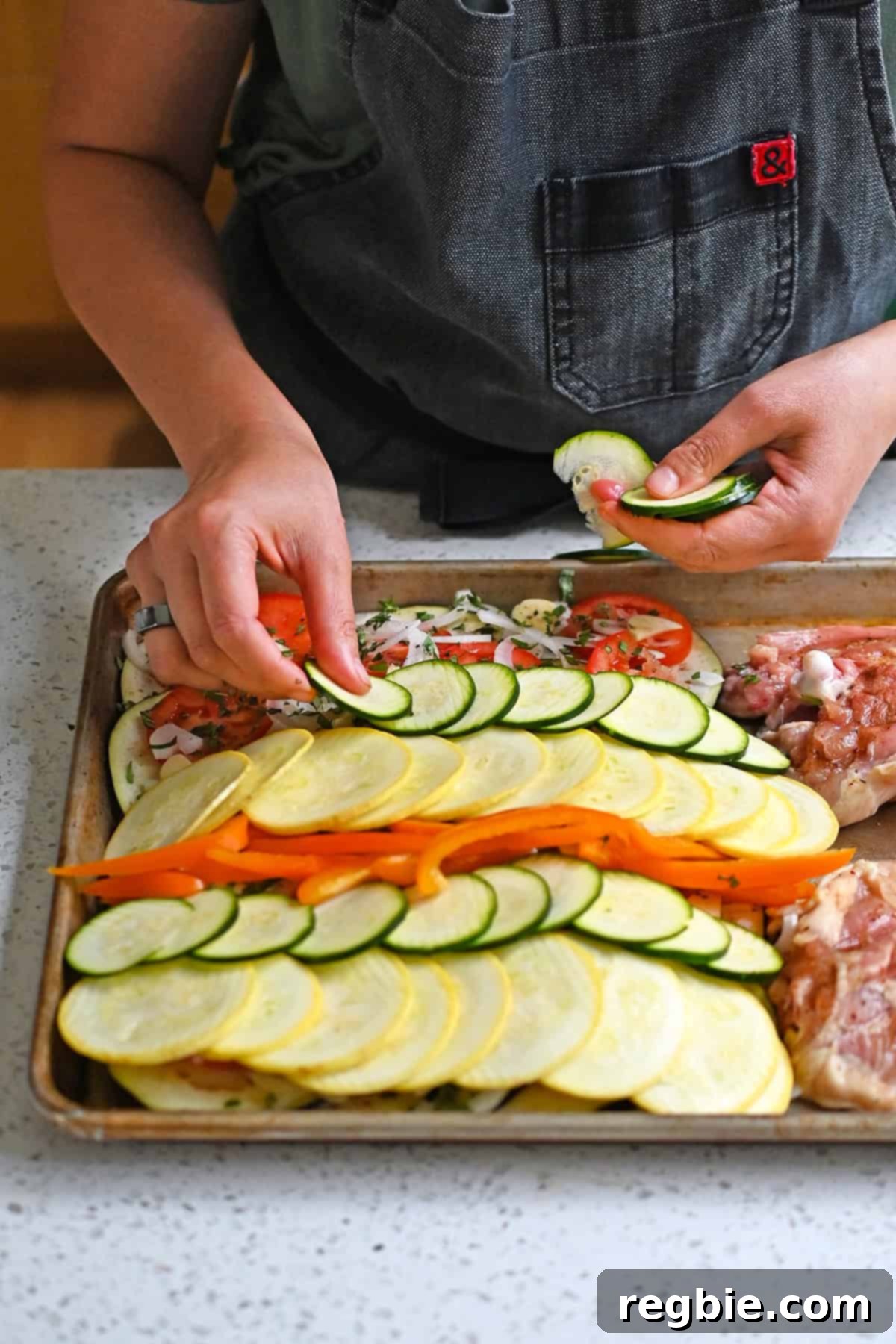 Adding a layer of thinly sliced yellow squash, zucchini, and bell pepper so that it has a colorful repeating pattern on a sheet pan.