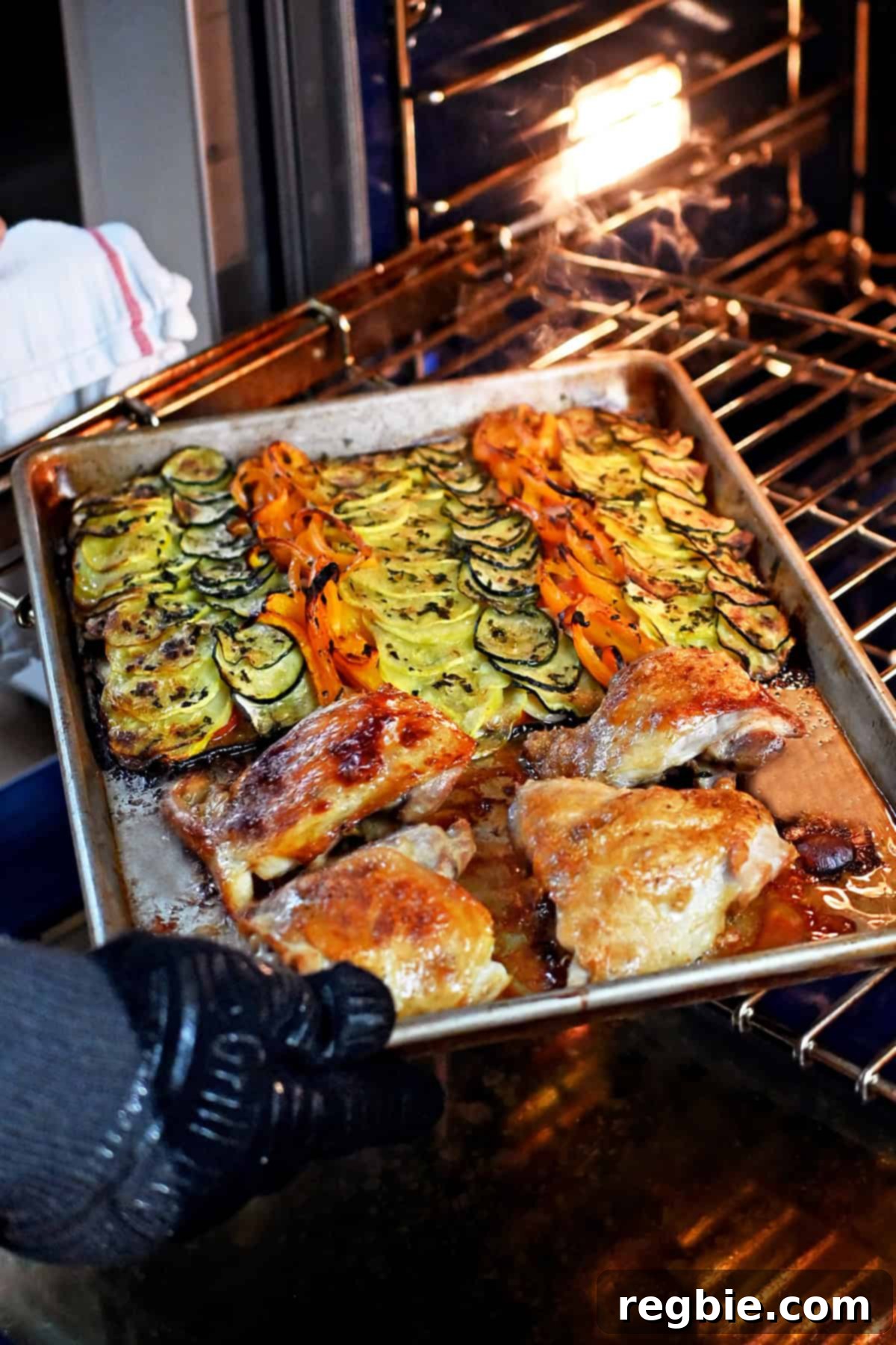 Removing a sheet pan with roasted ratatouille vegetables and golden brown chicken thighs from the oven.