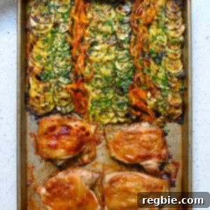 An overhead shot of two hands holding a sheet pan with roasted chicken and ratatouille vegetables topped with fresh herbs and aged balsamic vinegar.