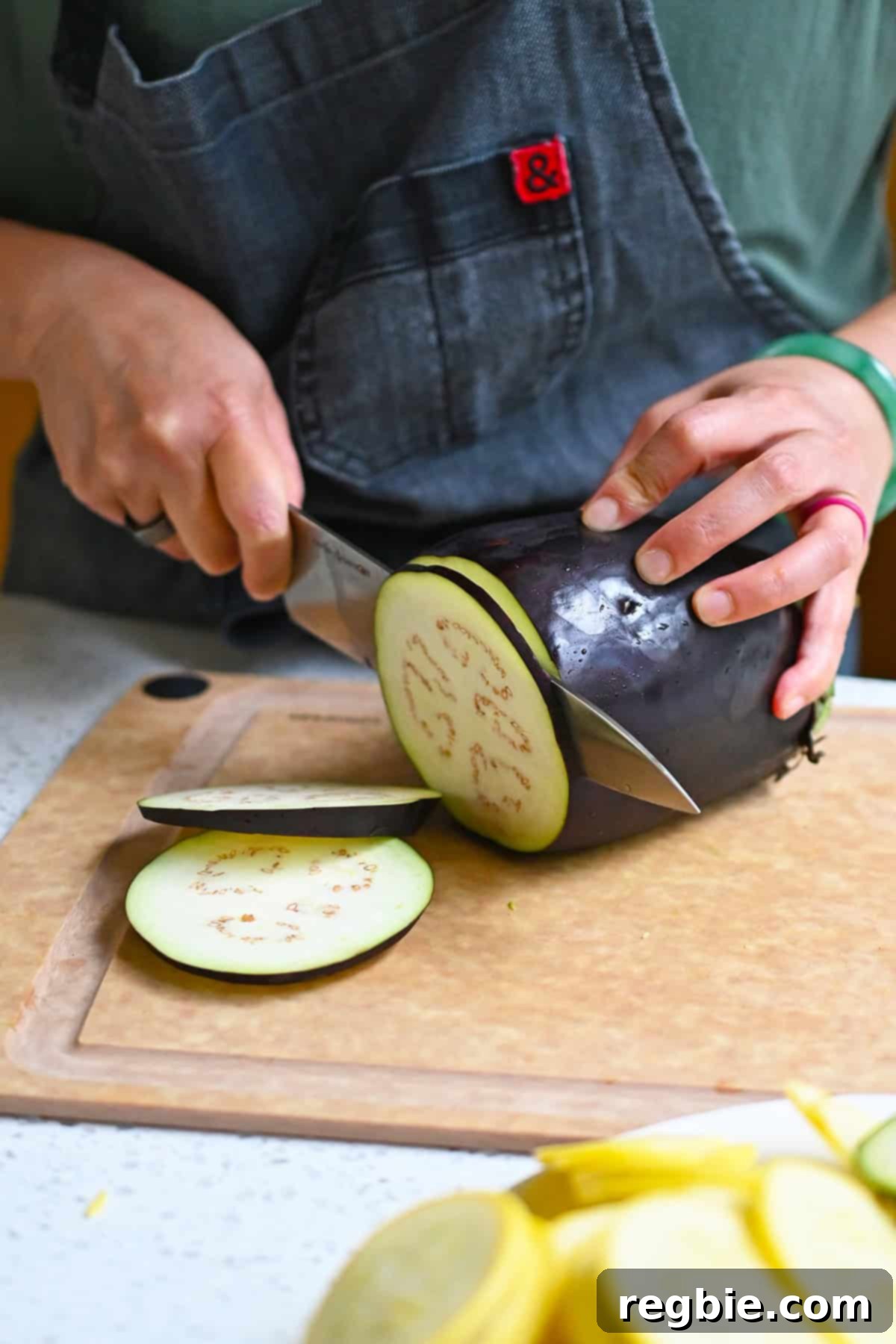 Thinly slicing a raw eggplant with a chef's knife on a cutting board.