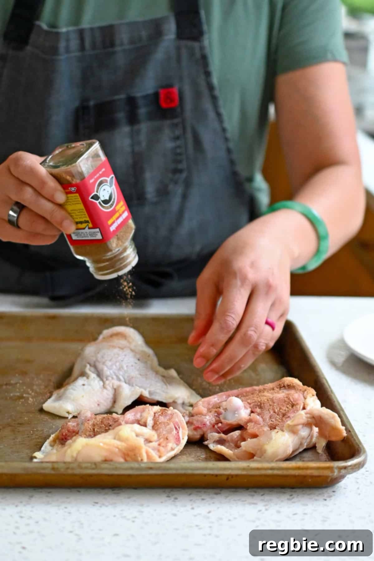 Sprinkling Magic Mushroom Powder on raw chicken thighs in a rimmed baking sheet.