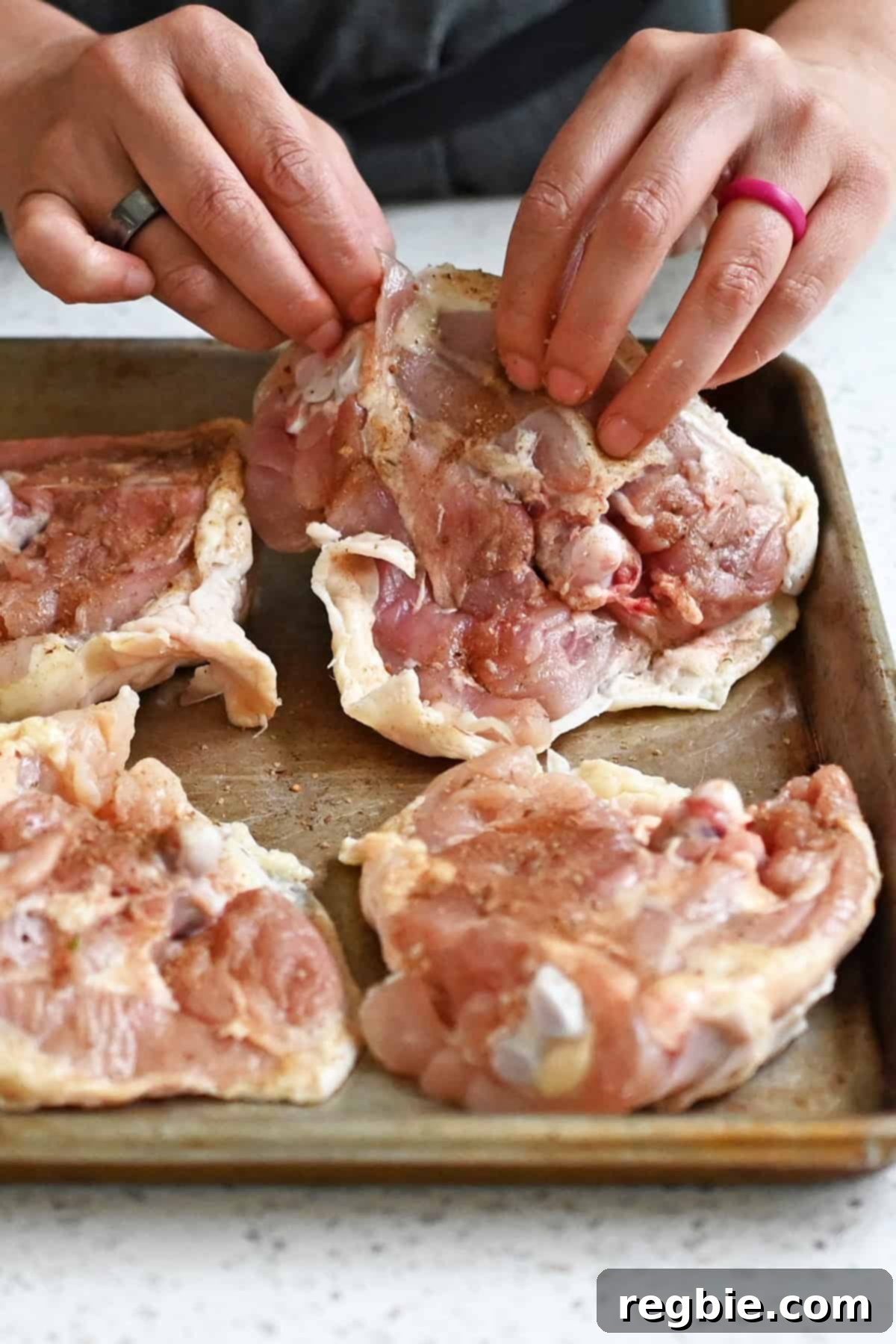 Placing four seasoned raw chicken thighs skin-side down on a rimmed baking sheet.