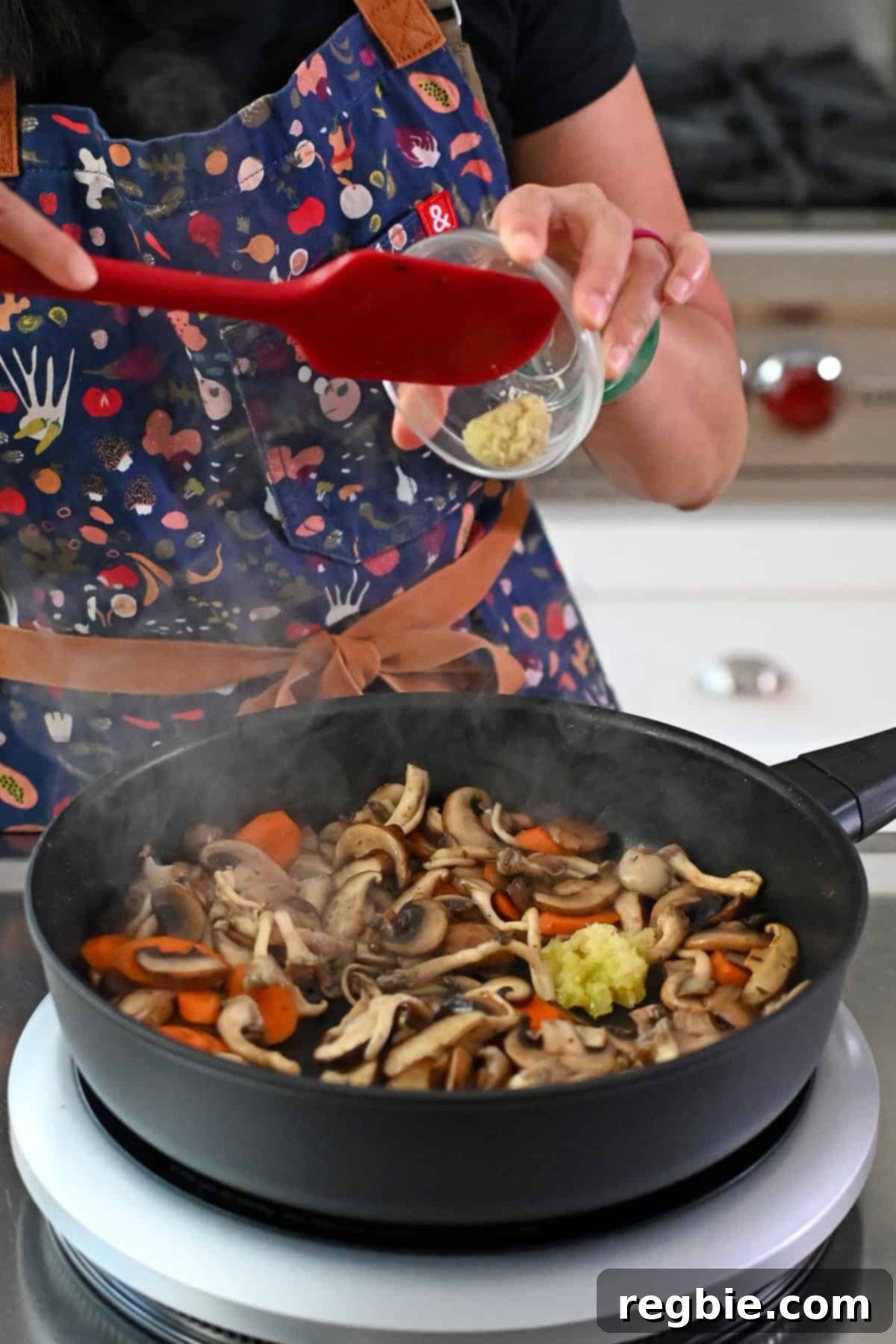 Cantonese Chicken and Mushroom Medley 17 Adding minced garlic and minced ginger to a frying pan with sautéed sliced mushrooms and carrots for moo goo gai pan.