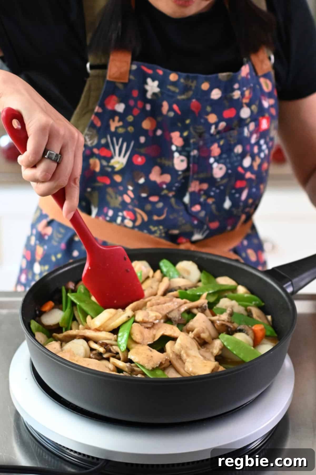 Cantonese Chicken and Mushroom Medley 21 A person in a colorful apron is cooking moo goo gai pan in a frying pan.