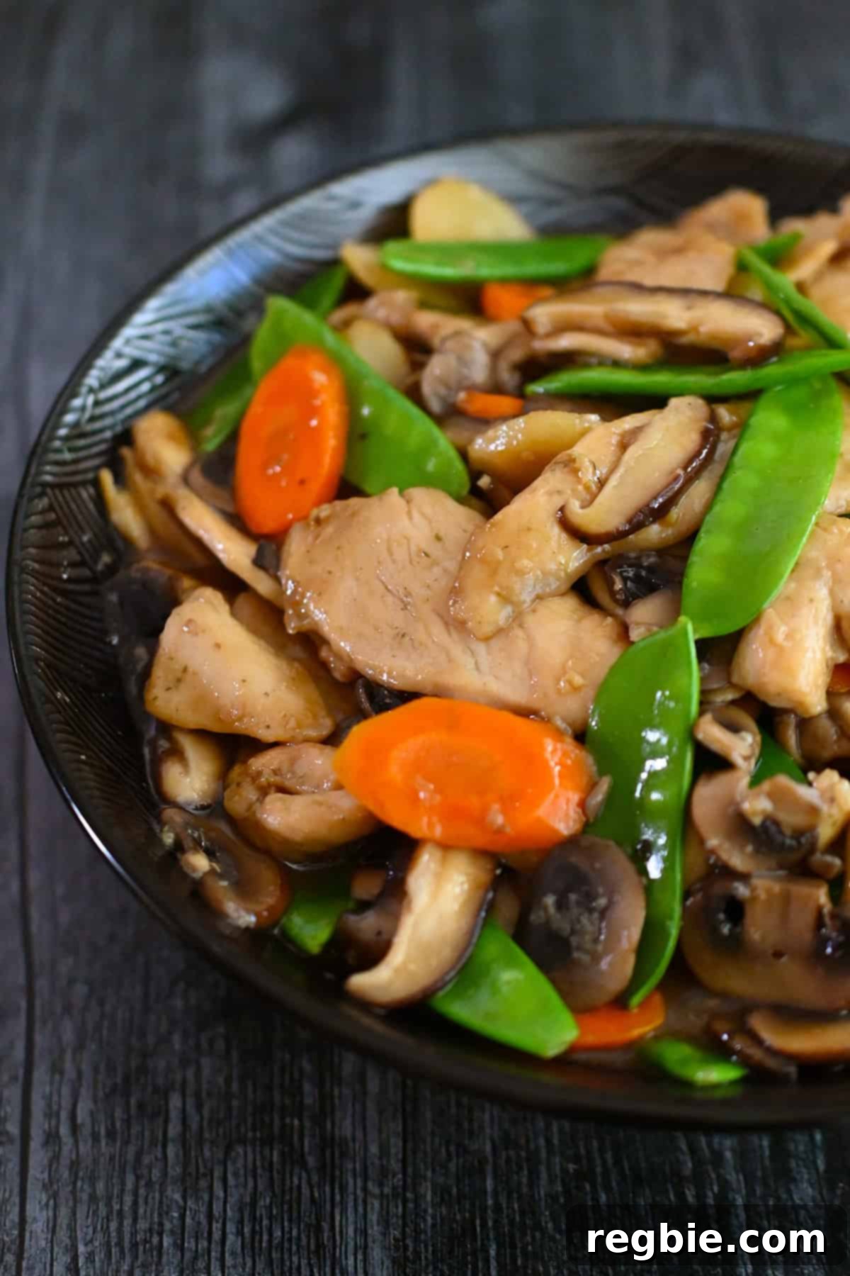 Cantonese Chicken and Mushroom Medley 22 A closeup overhead shot of half a bowl filled with stir fried chicken and mushrooms, moo goo gai pan.