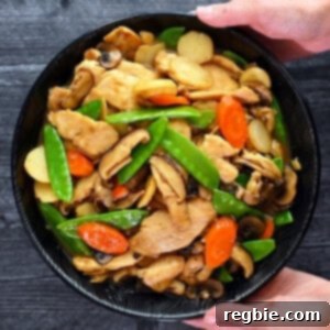 An overhead shot of two hands holding a black porcelain bowl filled with homemade stir fried chicken and mushrooms, moo goo gai pan.