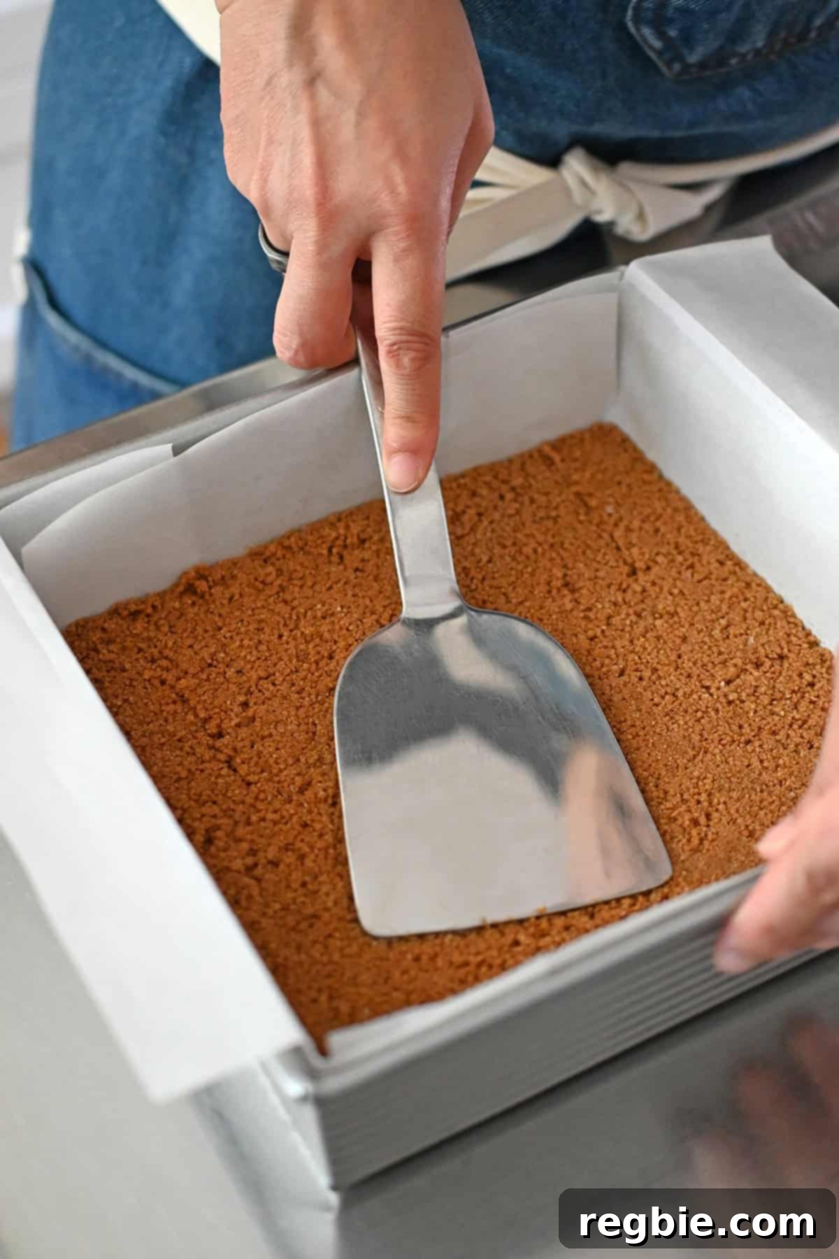 Golden Harvest Pumpkin Bars 13 Using a metal spatula to press down the cookie crumb crust into a parchment paper lined square metal baking pan.