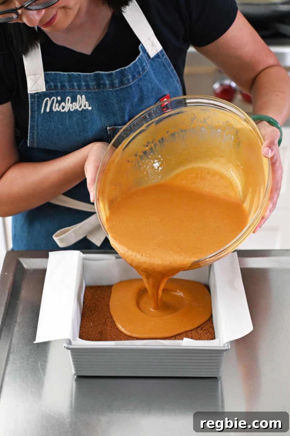 Golden Harvest Pumpkin Bars 20 A smiling Asian woman is pouring the pumpkin pie bar batter into a square pan filled with a par-baked cookie crust.
