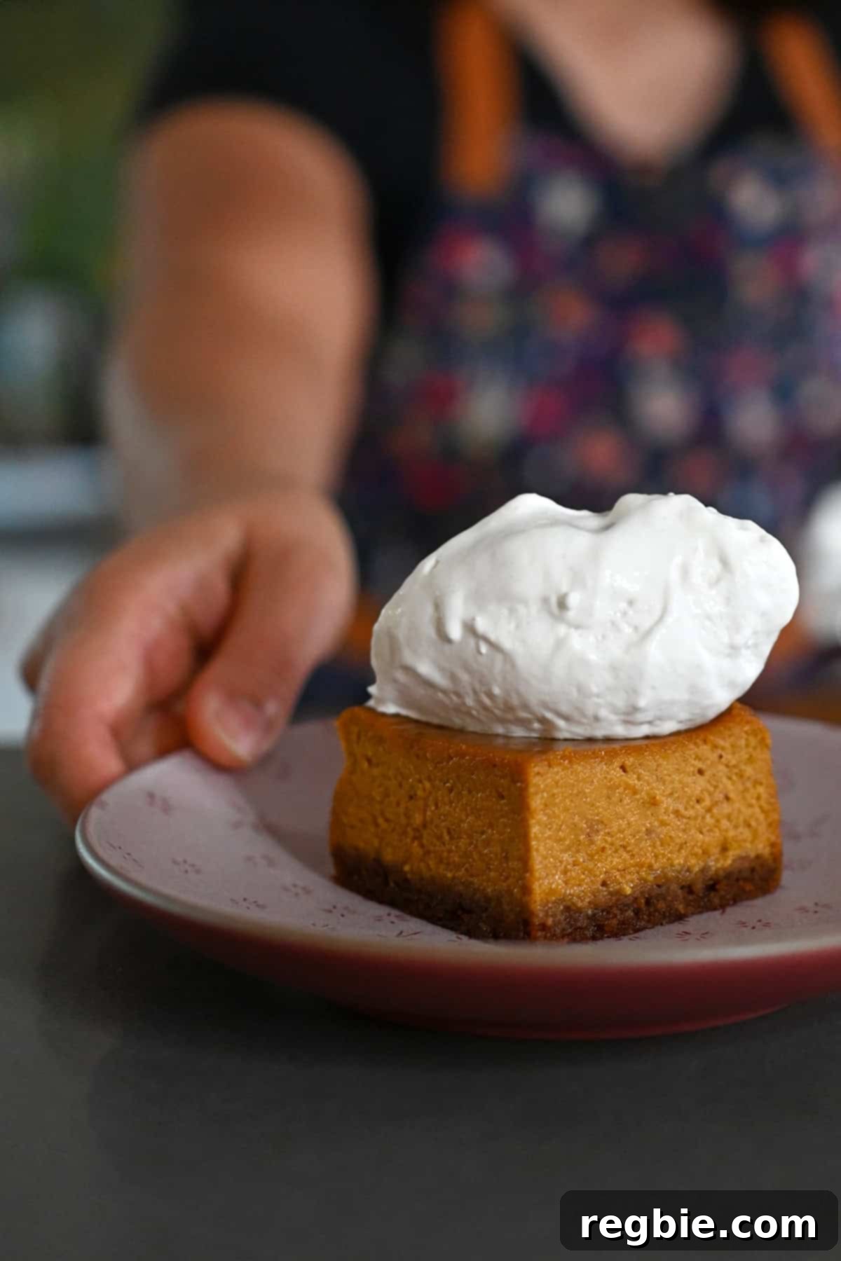 Golden Harvest Pumpkin Bars 25 A hand is holding a small pink plate topped with a square of pumpkin pie bar with whipped coconut cream on top.