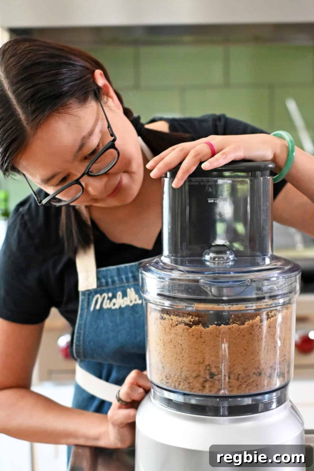 Golden Harvest Pumpkin Bars 9 An Asian woman in glasses is pulsing grain-free cookies into crumbs in a food processor for pumpkin pie bars.