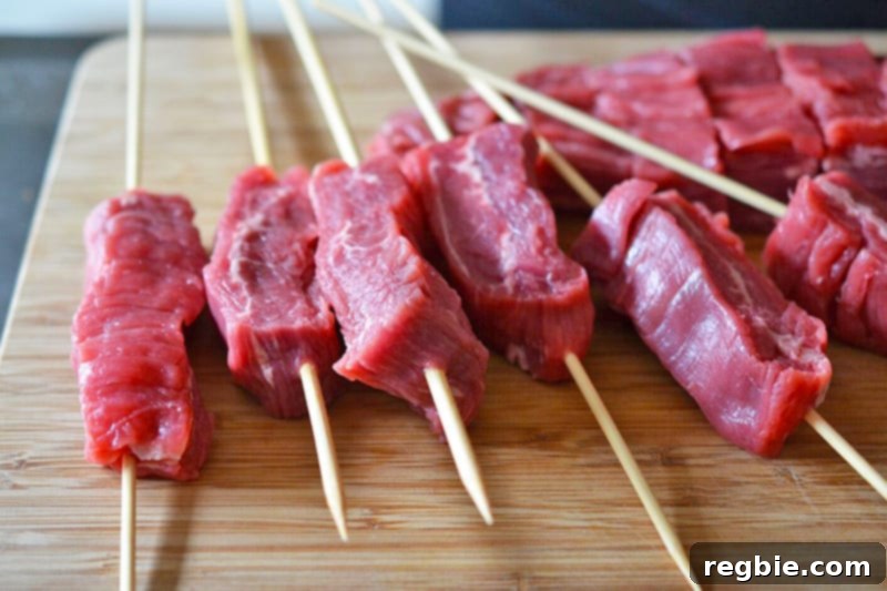 A wooden cutting board has a bunch of flank steak kabobs waiting for the barbecue.