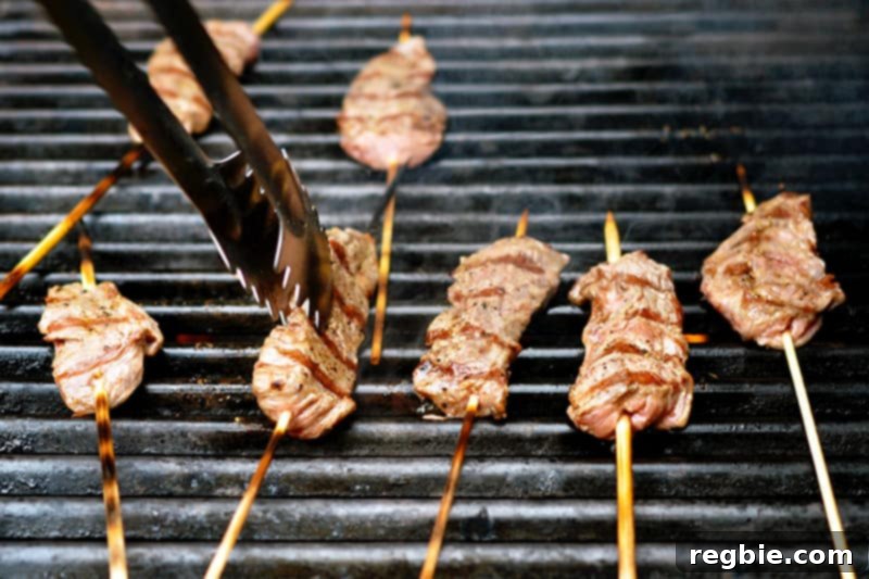 Fully cooked Whole30-friendly smashed steak skewers are removed from the grill with tongs.