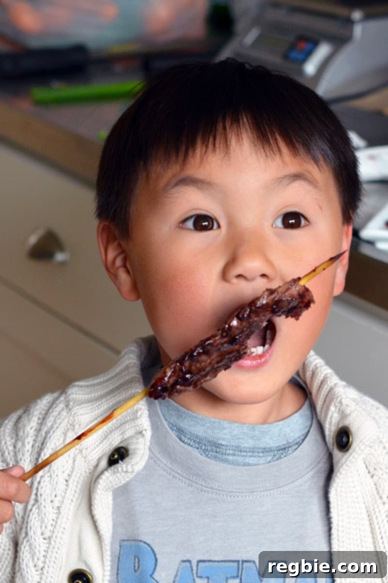 A little Asian boy is biting into a grilled beef kabob with Whole30 BBQ sauce