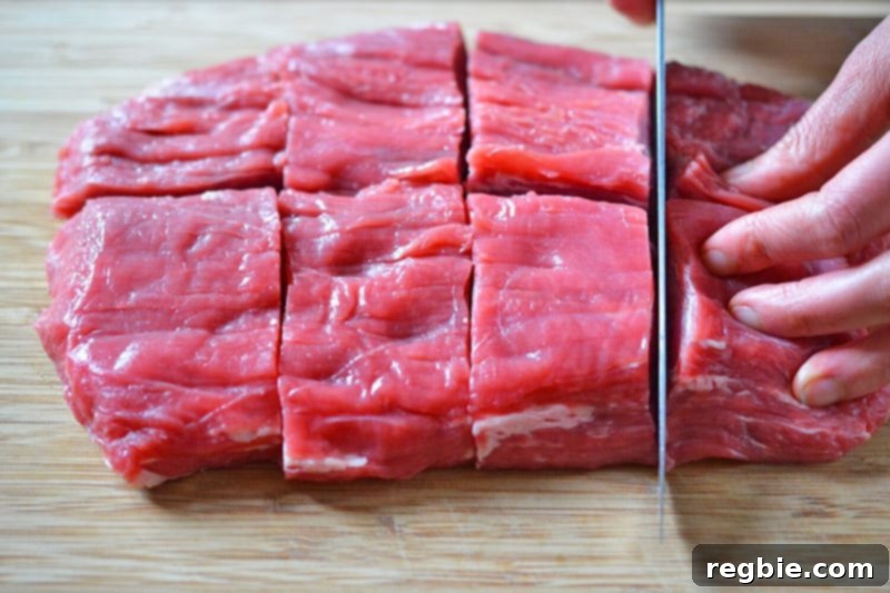 Someone is using a chef's knife to slice up flank steak into even pieces.