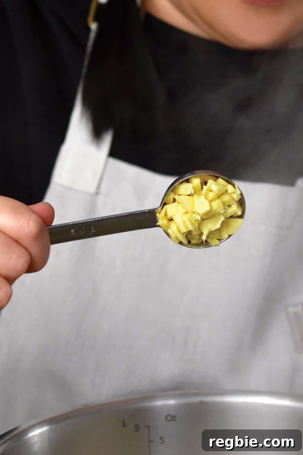 A spoonful of chopped fresh ginger being added to the Instant Pot with sautéed onions and garlic, enhancing the aromatic base of the green soup.