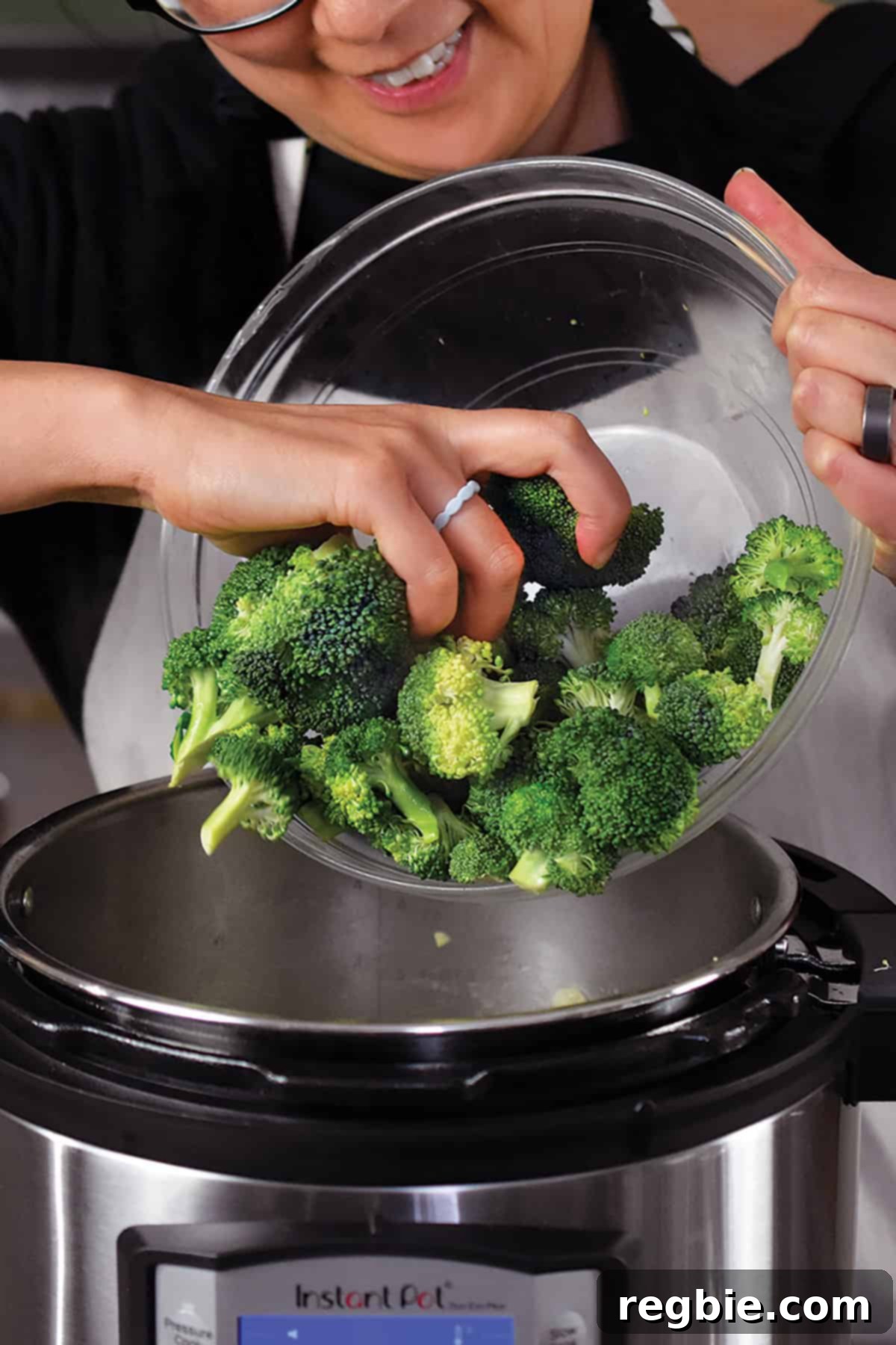 Chopped broccoli florets being added into an open Instant Pot, joining the sautéed aromatics for the green soup.