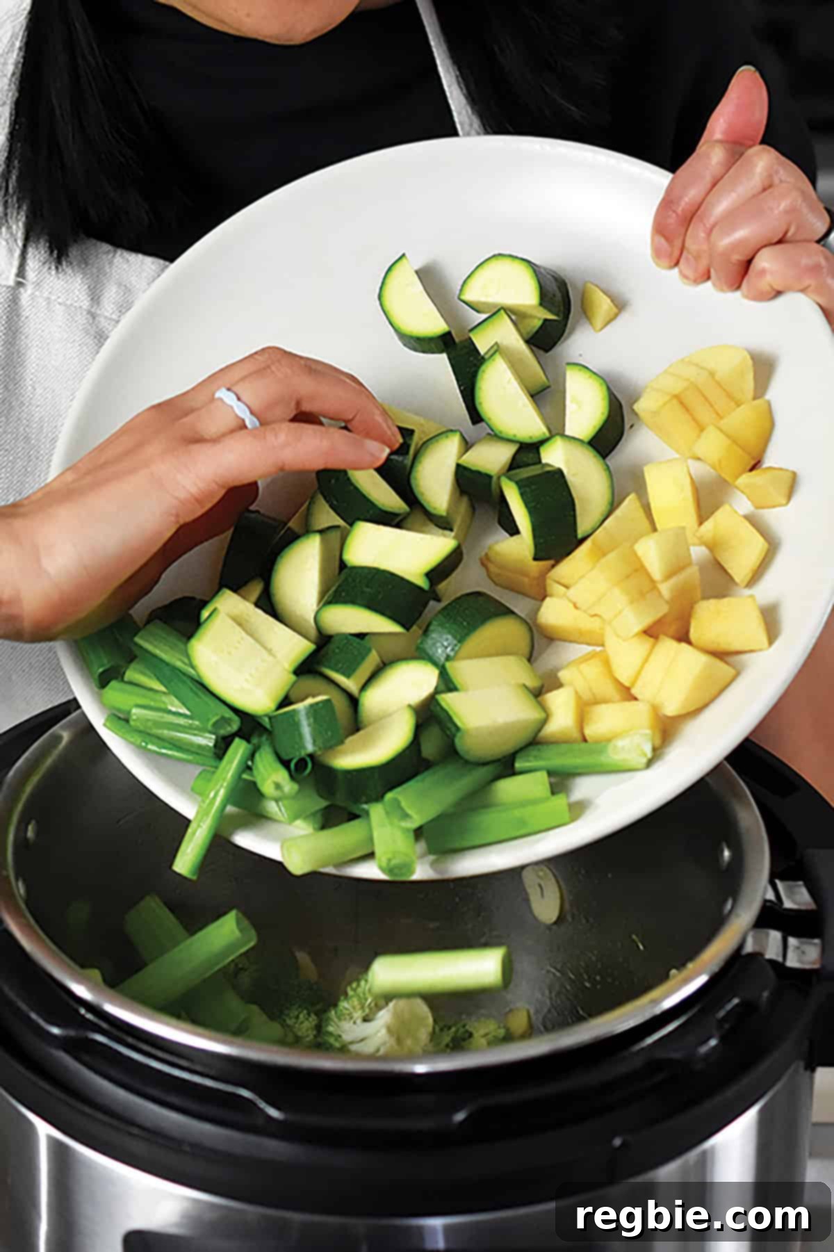 Chopped zucchini, green onions, and diced apples being added to the Instant Pot, completing the vegetable mix for the green soup.