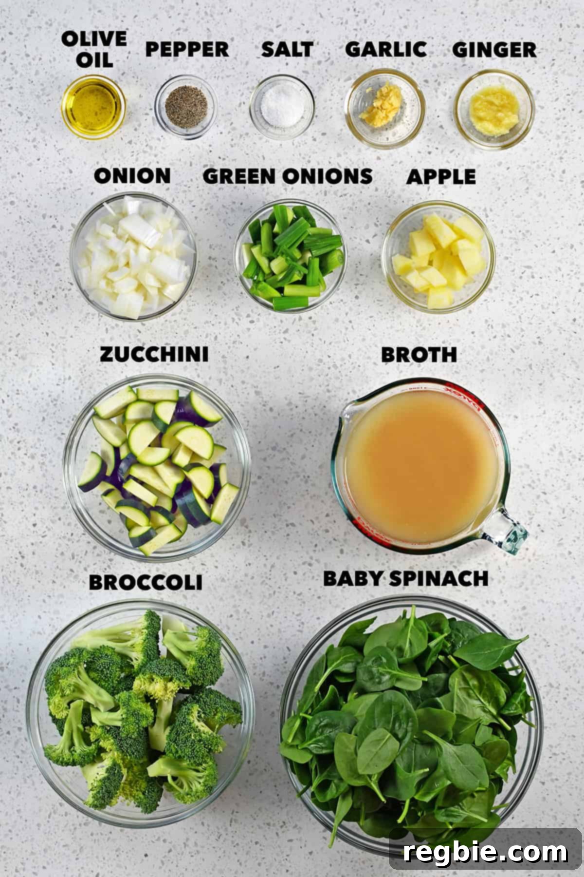 A beautiful overhead shot of fresh, raw ingredients meticulously arranged for the green soup, including broccoli, zucchini, onions, and spinach.
