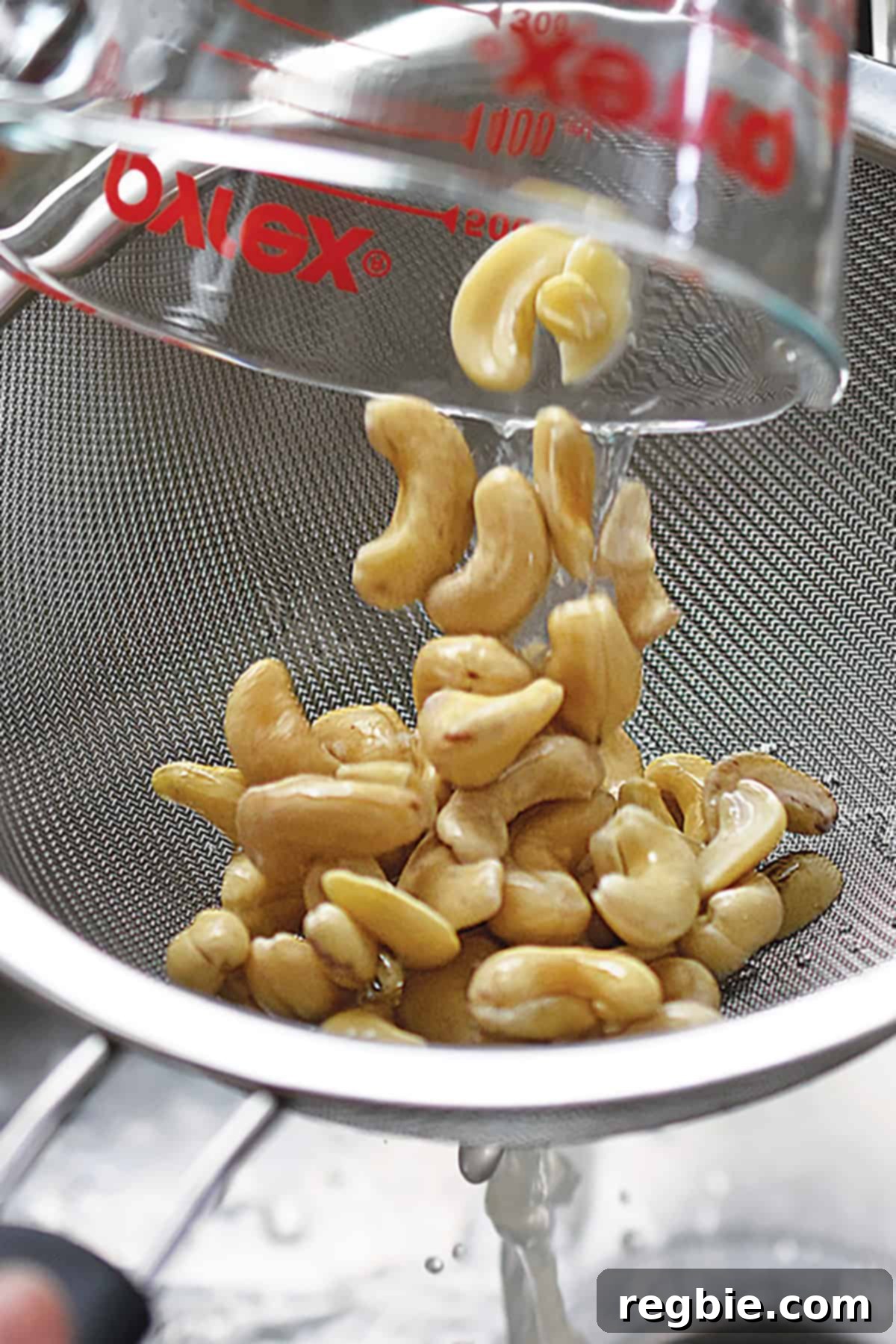 Raw cashews being poured from a strainer into a high-speed blender, ready for making the creamy cashew topping.
