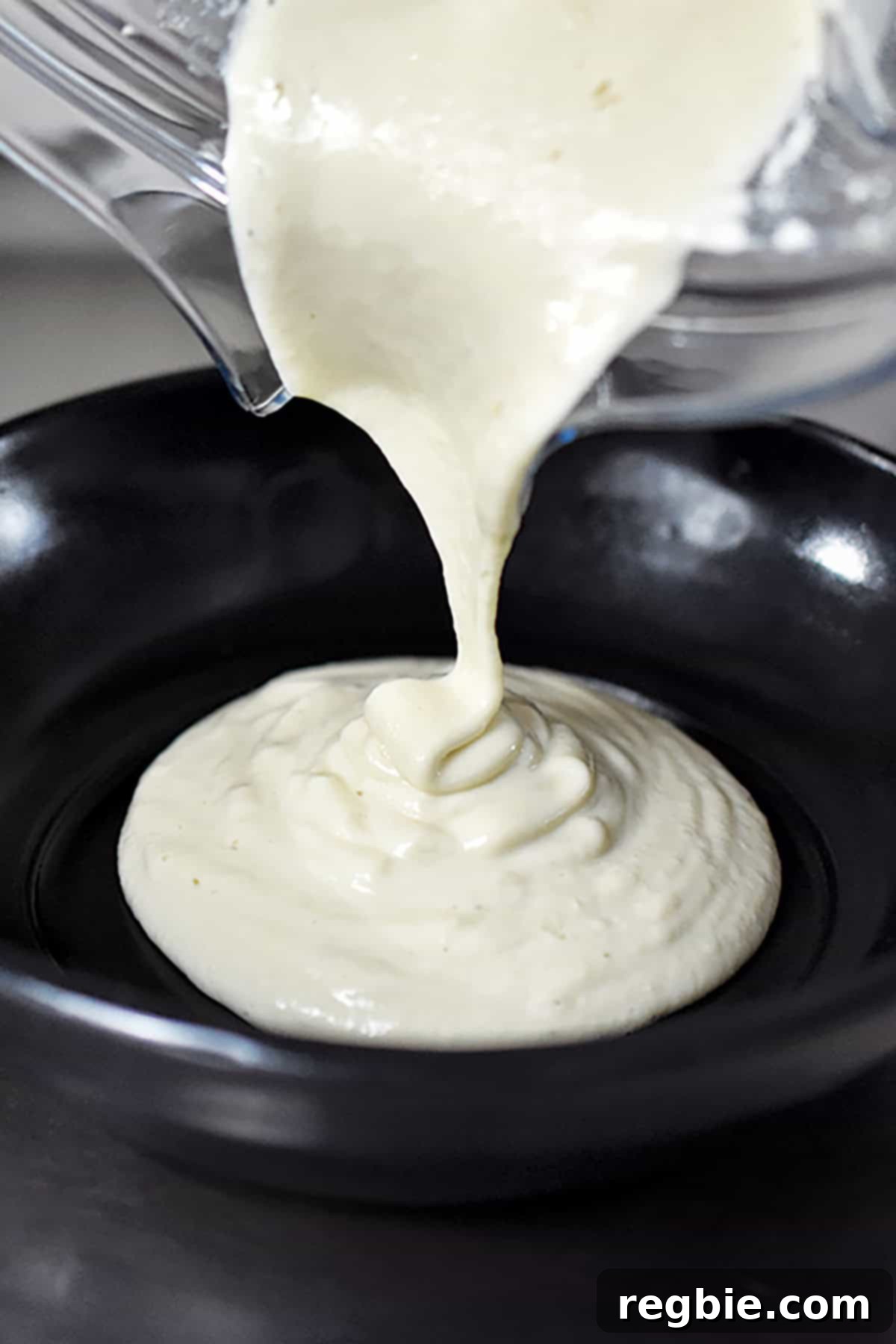 The creamy dairy-free cashew cream being poured from the Vitamix blender into a small white serving bowl, showcasing its smooth texture.