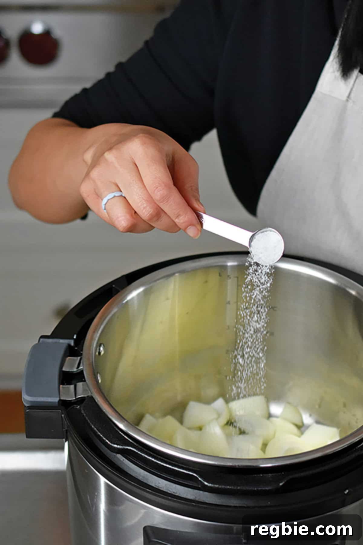 A spoonful of kosher salt being sprinkled over chopped onions in an open Instant Pot, beginning the sauté process.