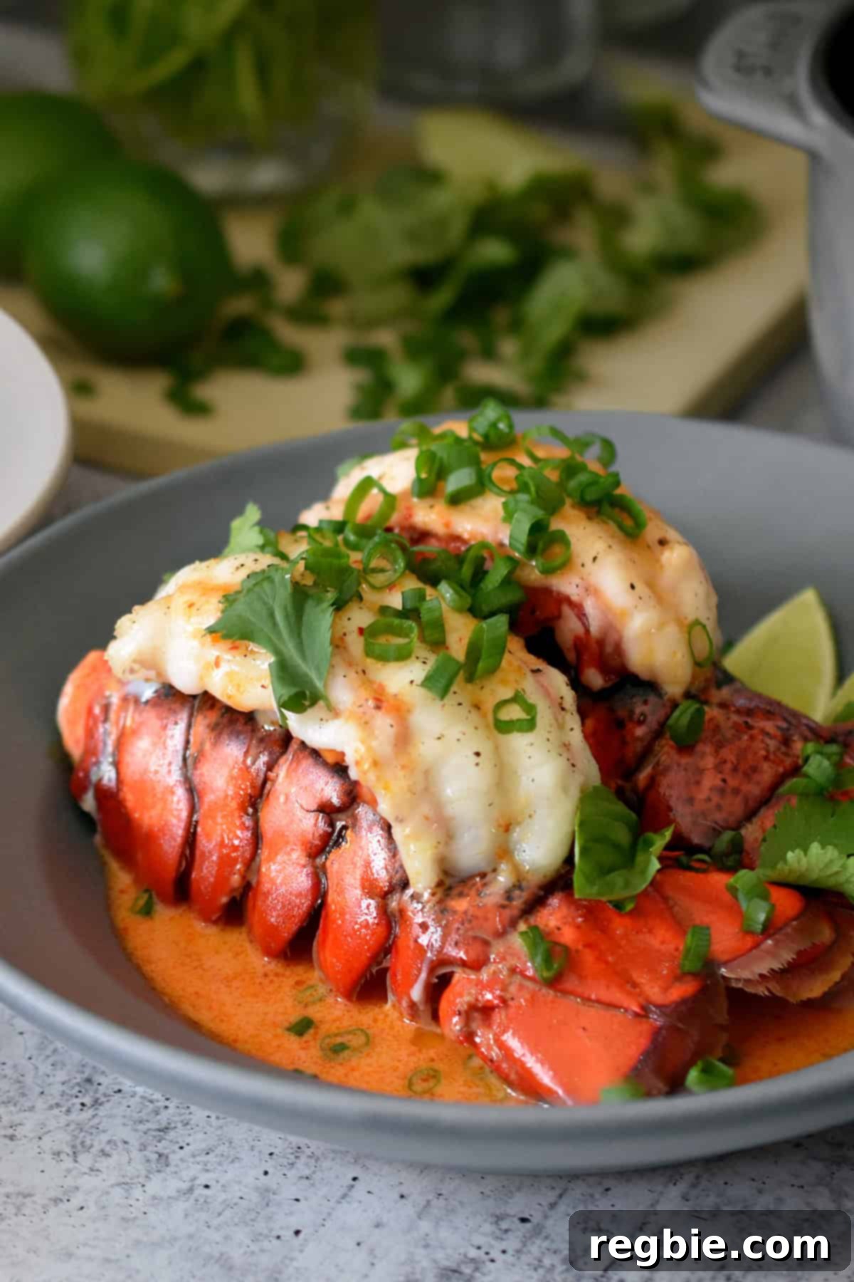 A closeup of a shallow gray bowl filled with baked lobster tails with Thai red curry sauce and topped with fresh herbs.