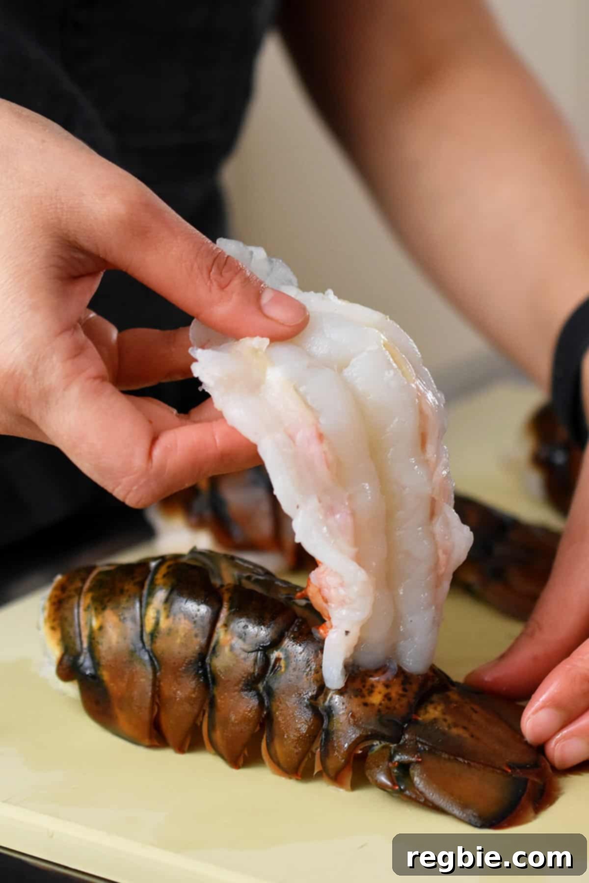 Using hands to carefully pull the lobster tail meat from inside the tail to the top of the shell, while keeping the end piece of the meat attached near the tail.