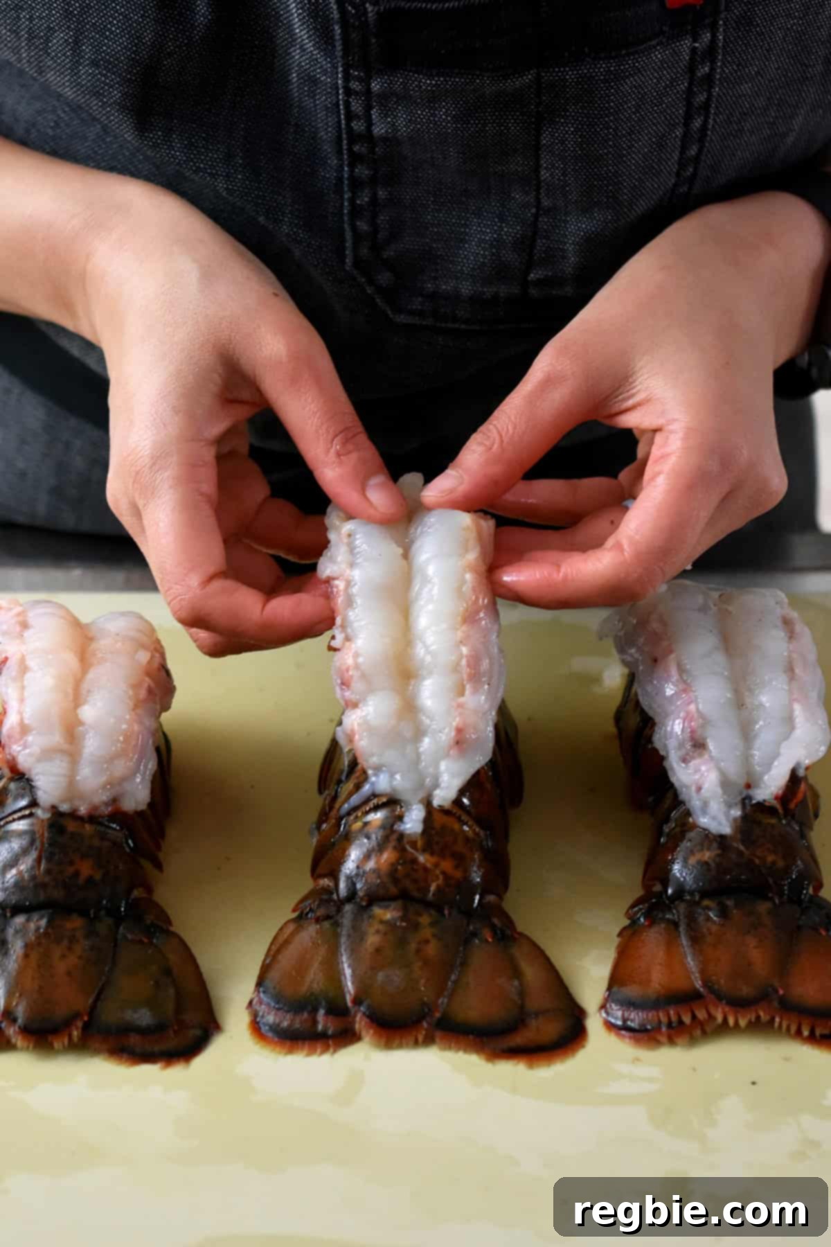 Arranging three butterflied raw lobster tails on a cutting board.