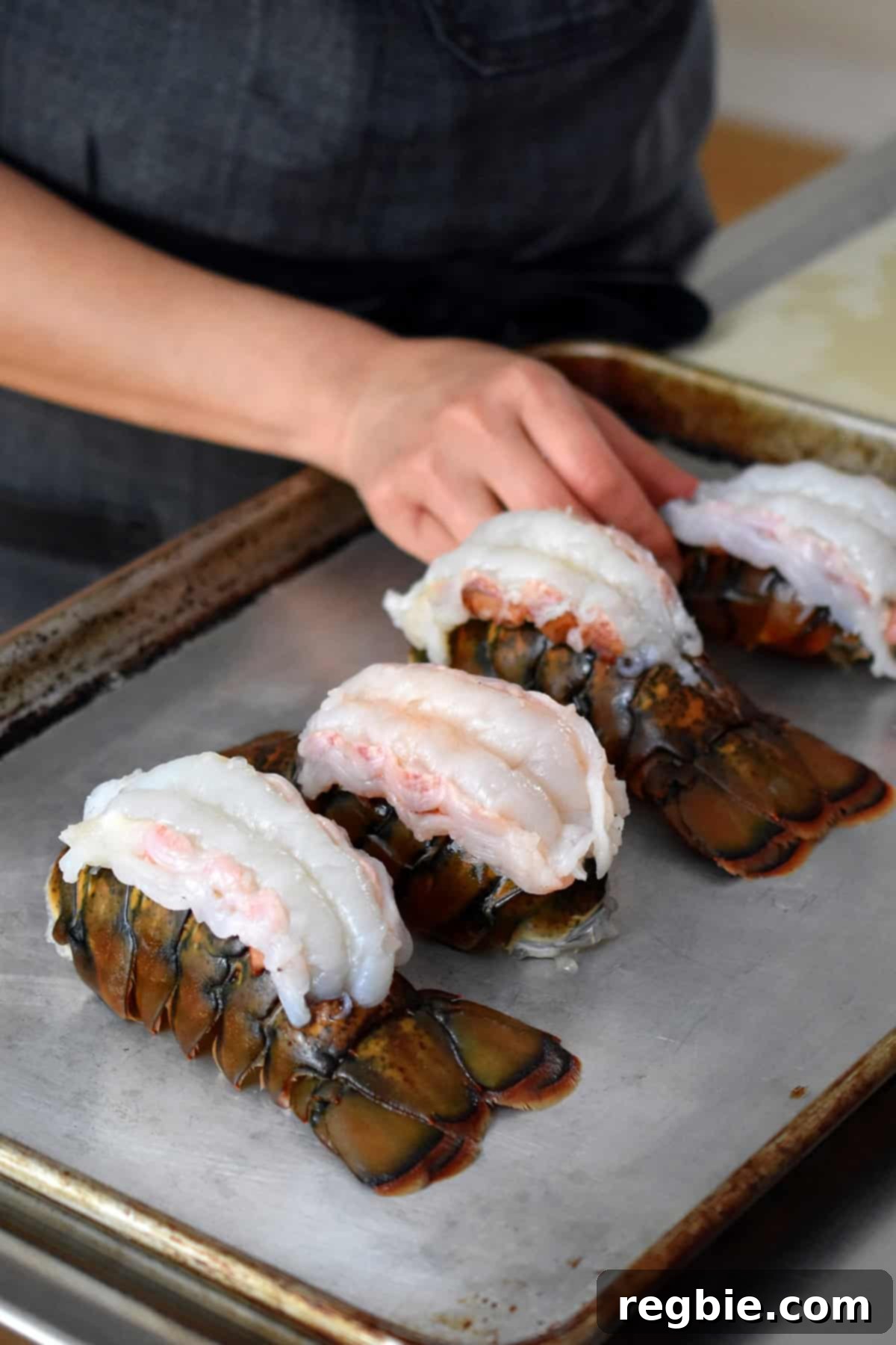 Arranging four raw butterflied lobster tails on a rimmed baking sheet.